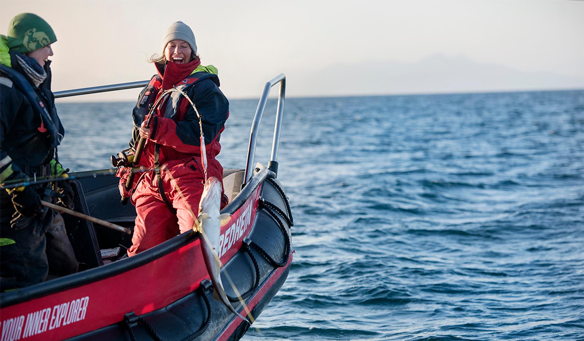 A guide next to a guest in a RIB boat where the guest is holding a fishing pole with a hooked fish hanging in the air next to the boat