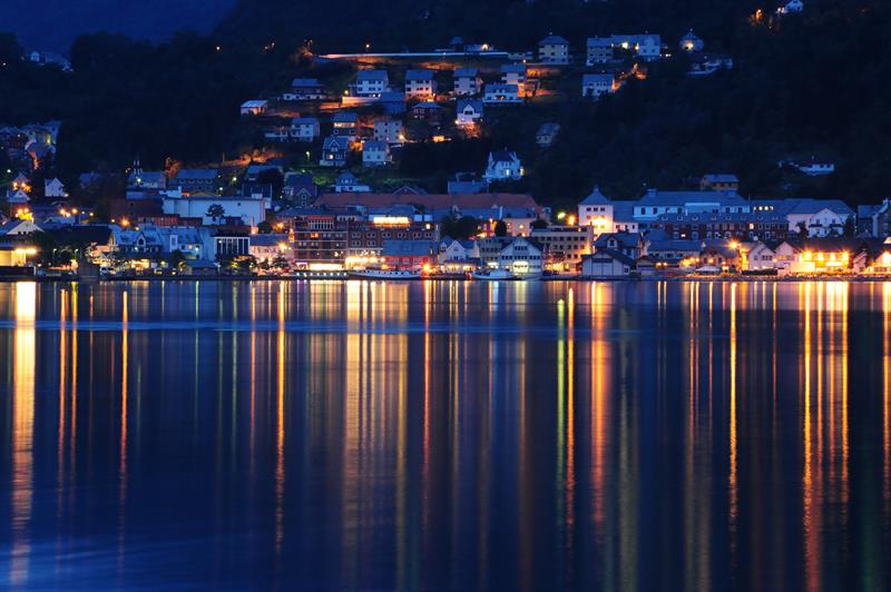Kveldslys over Odda og Hardanger Hotel speglar seg i stille fjordvatn.