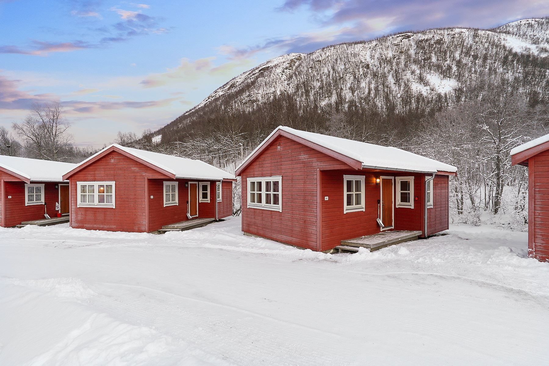 Red cabins in a snowy landscape with mountains and colourful sky in the background
