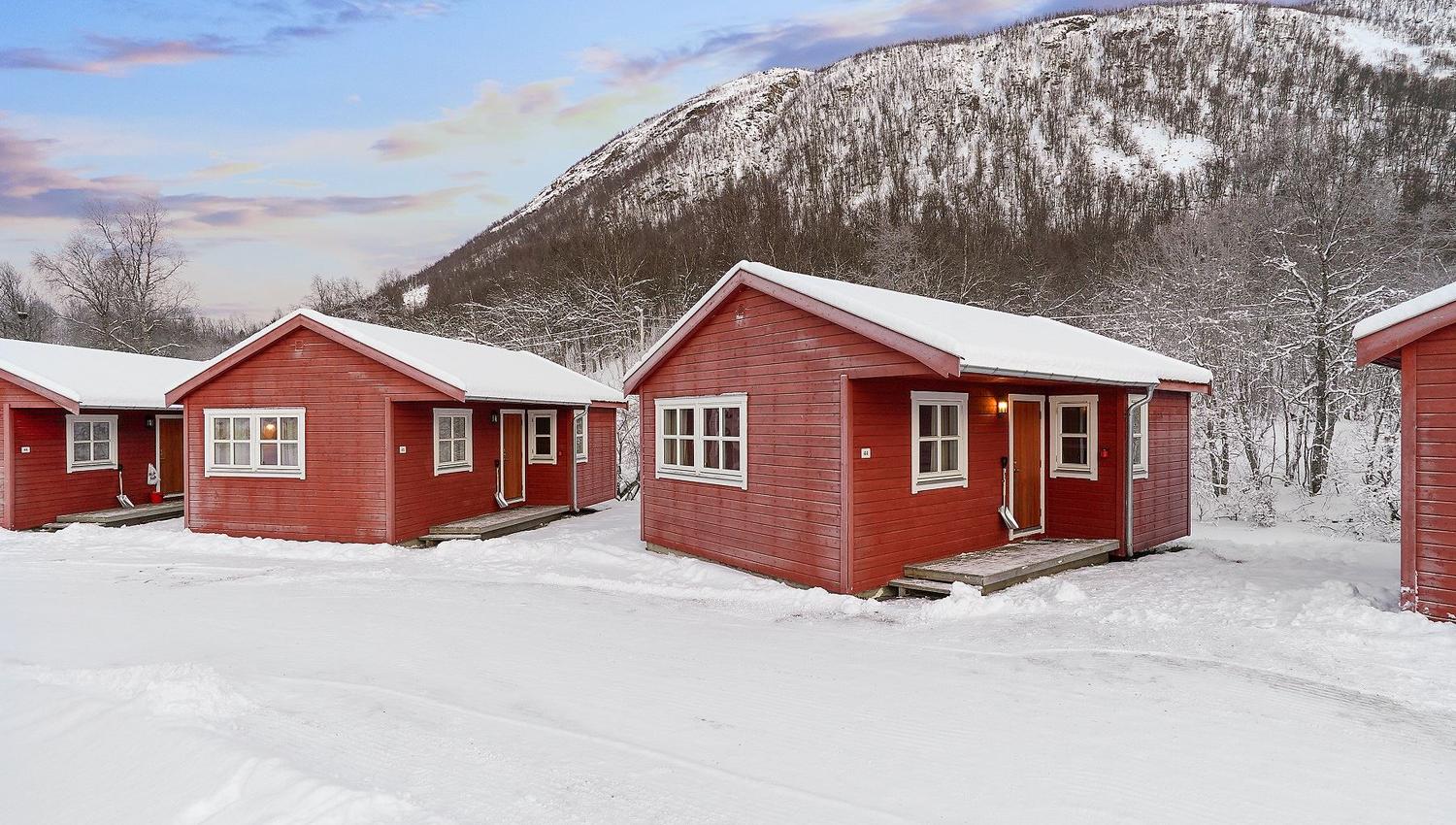 Red cabins in a snowy landscape with mountains and colourful sky in the background