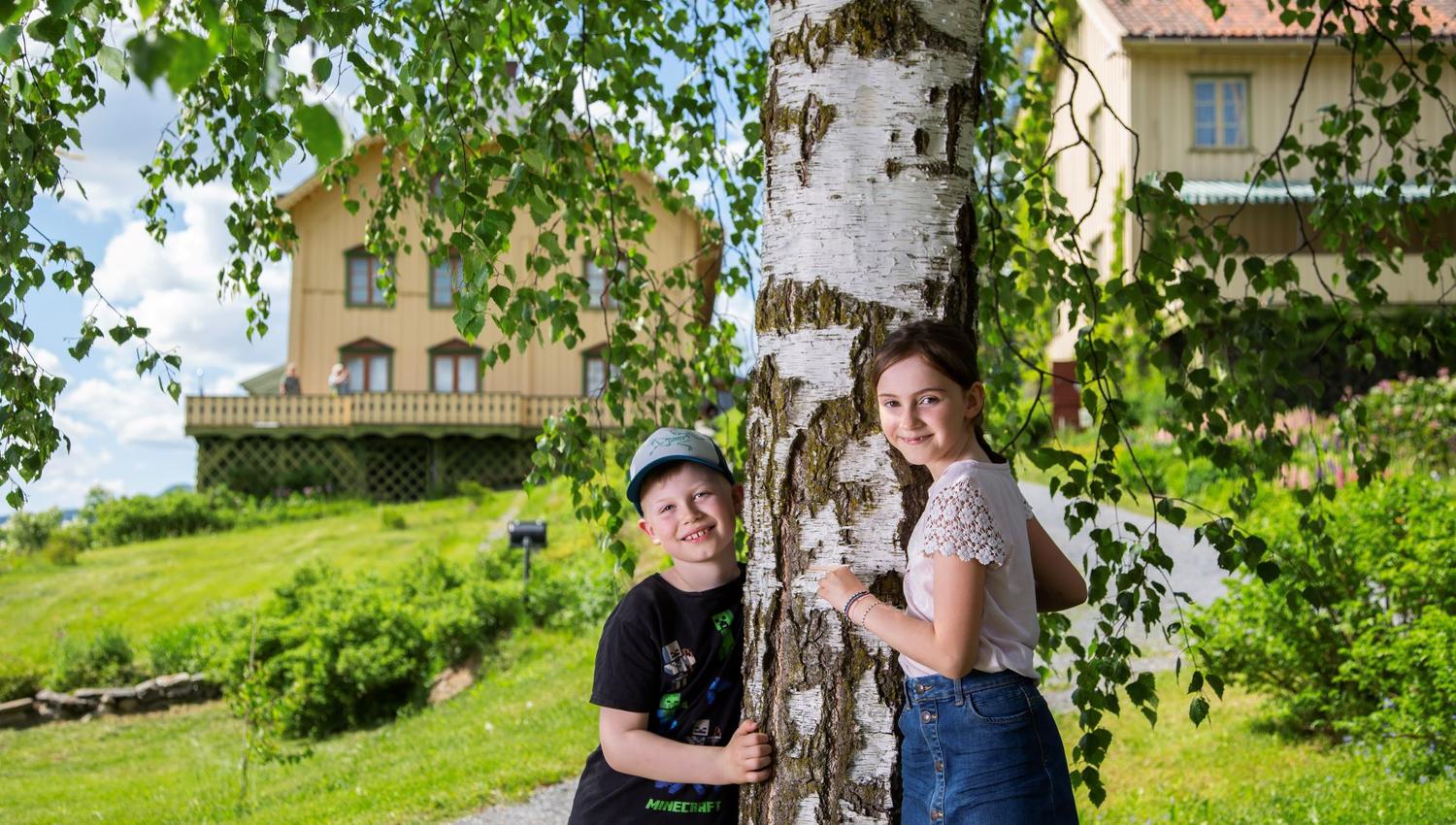 En gutt og en jente som lener seg mot et tre.