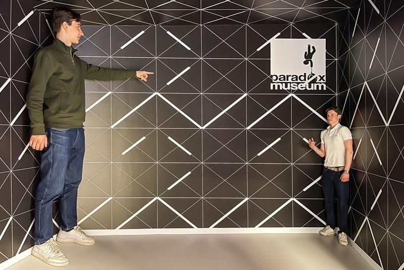 Svart rom med to gutter i forskjellig perspektiv; den ene er stor den andre liten.