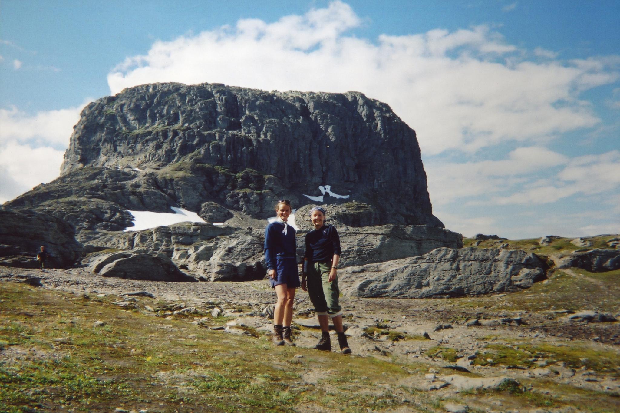 To turgåarar på Hardangervidda med majestetisk fjellformasjon i bakgrunnen under klar sommarhimmel.