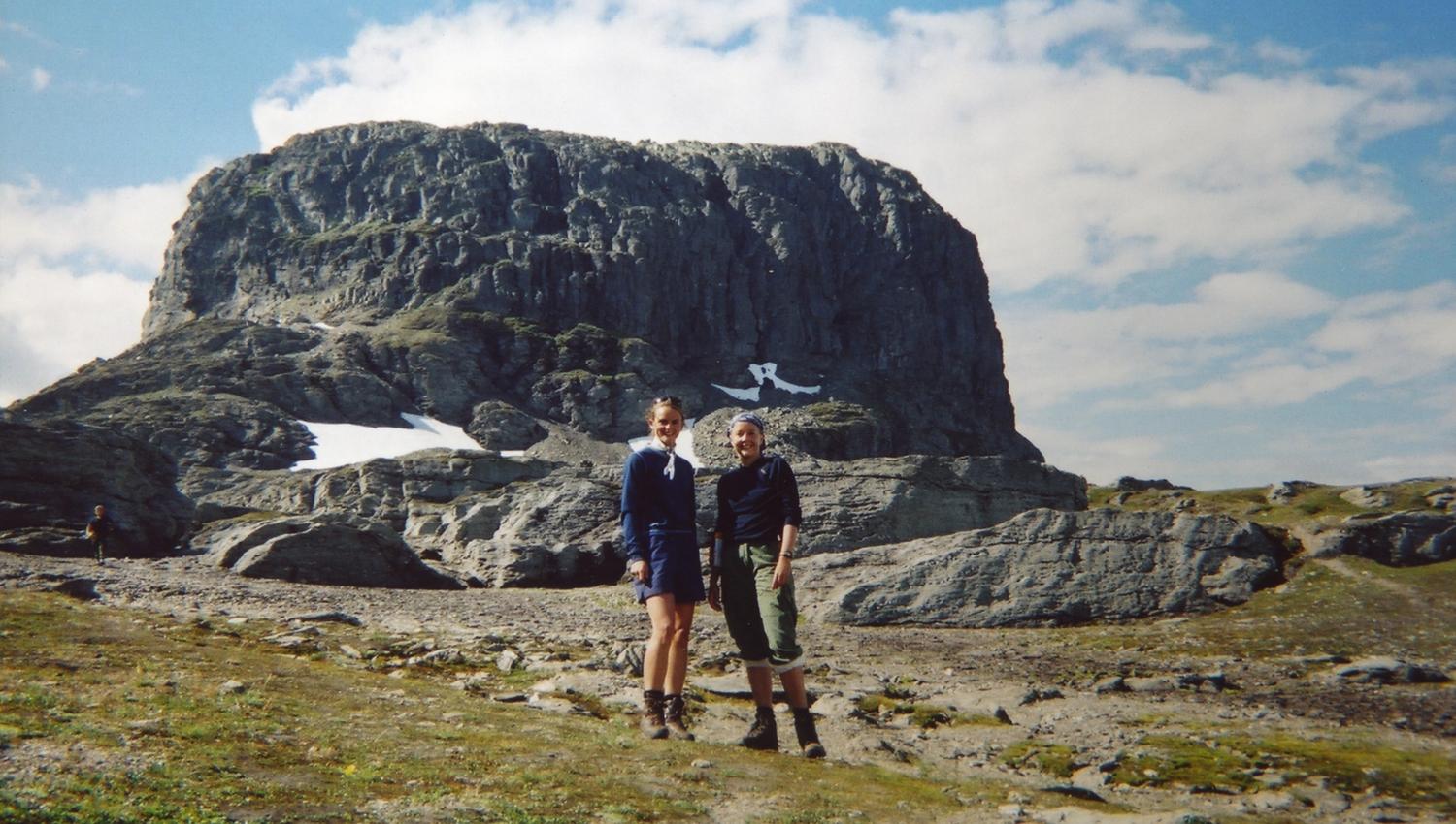 Two hikers on the Hardangervidda plateau with a dramatic mountain formation in the background on a clear summer day.