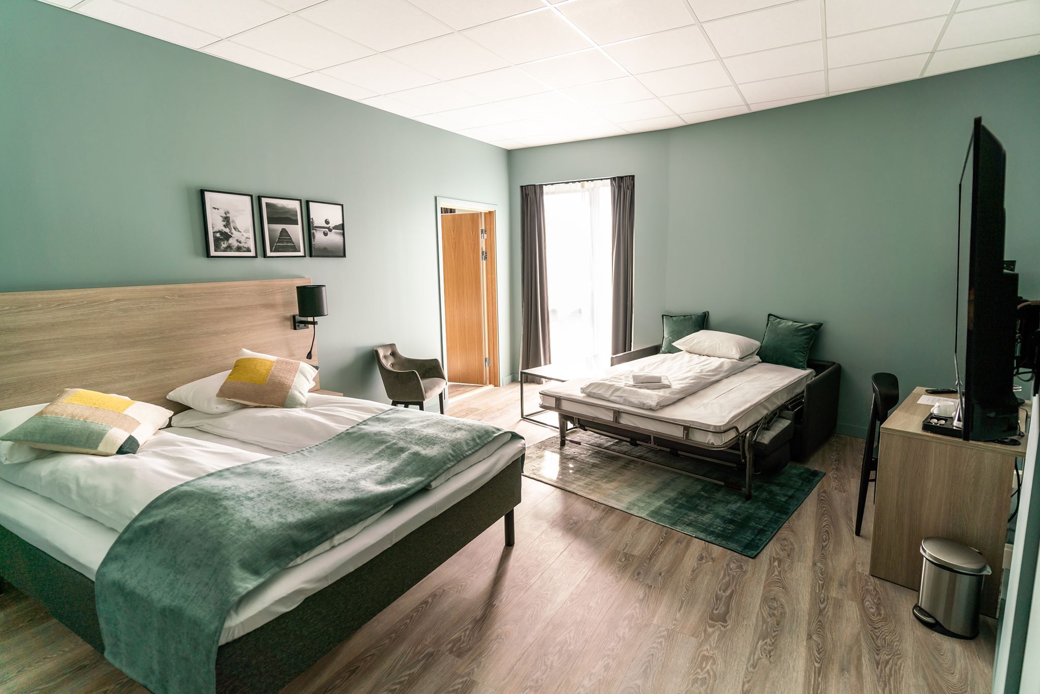 Romslig hotellrom med dobbeltseng, enkeltseng og moderne interiør.