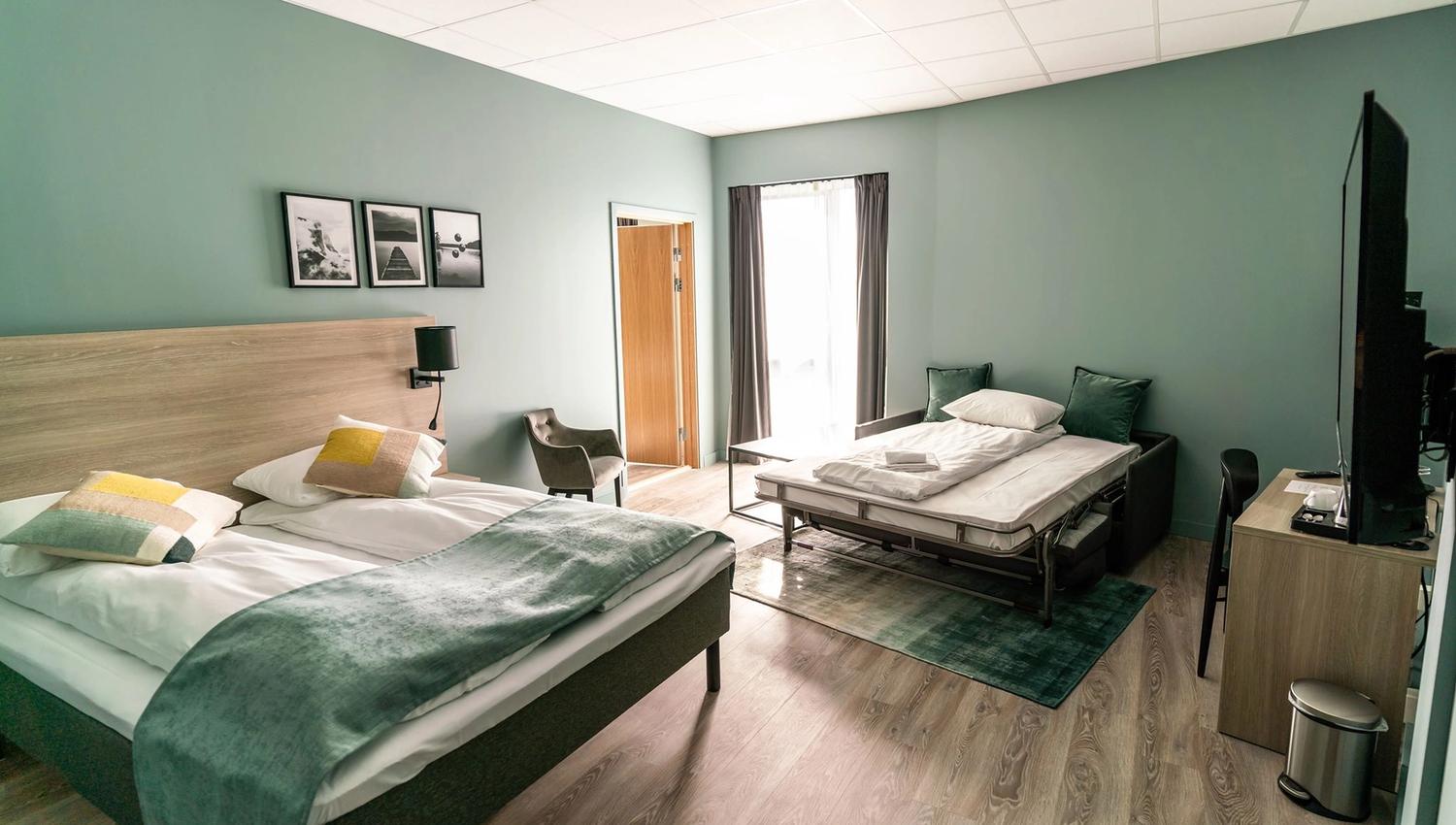 Romslig hotellrom med dobbeltseng, enkeltseng og moderne interiør.