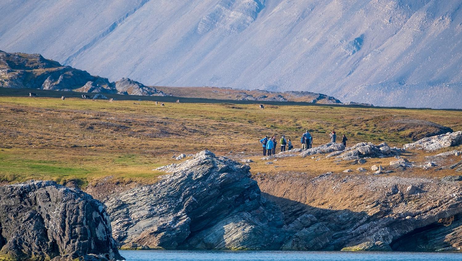 A guided group of people standing on a small cliff by a fjord
