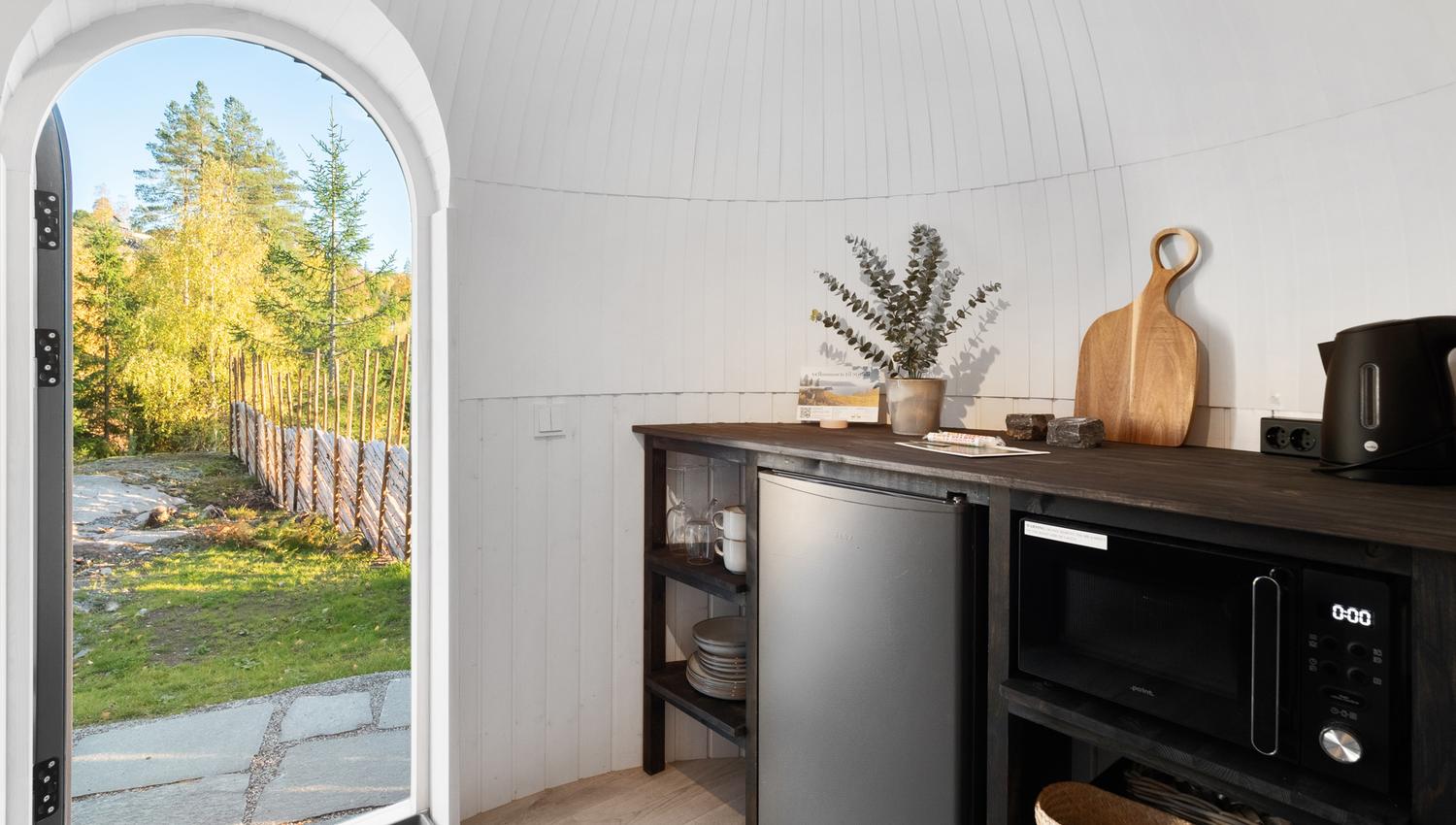 Lite kjøkken med en dør som står åpen med utsikt mot et gjerde og grønn skog