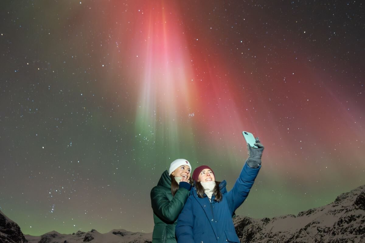 Et par tar en selfie med rødt nordlys i bakgrunnen