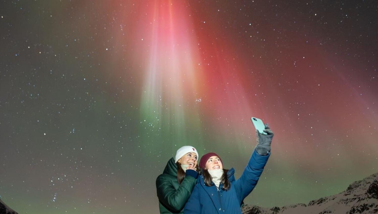 Et par tar en selfie med rødt nordlys i bakgrunnen