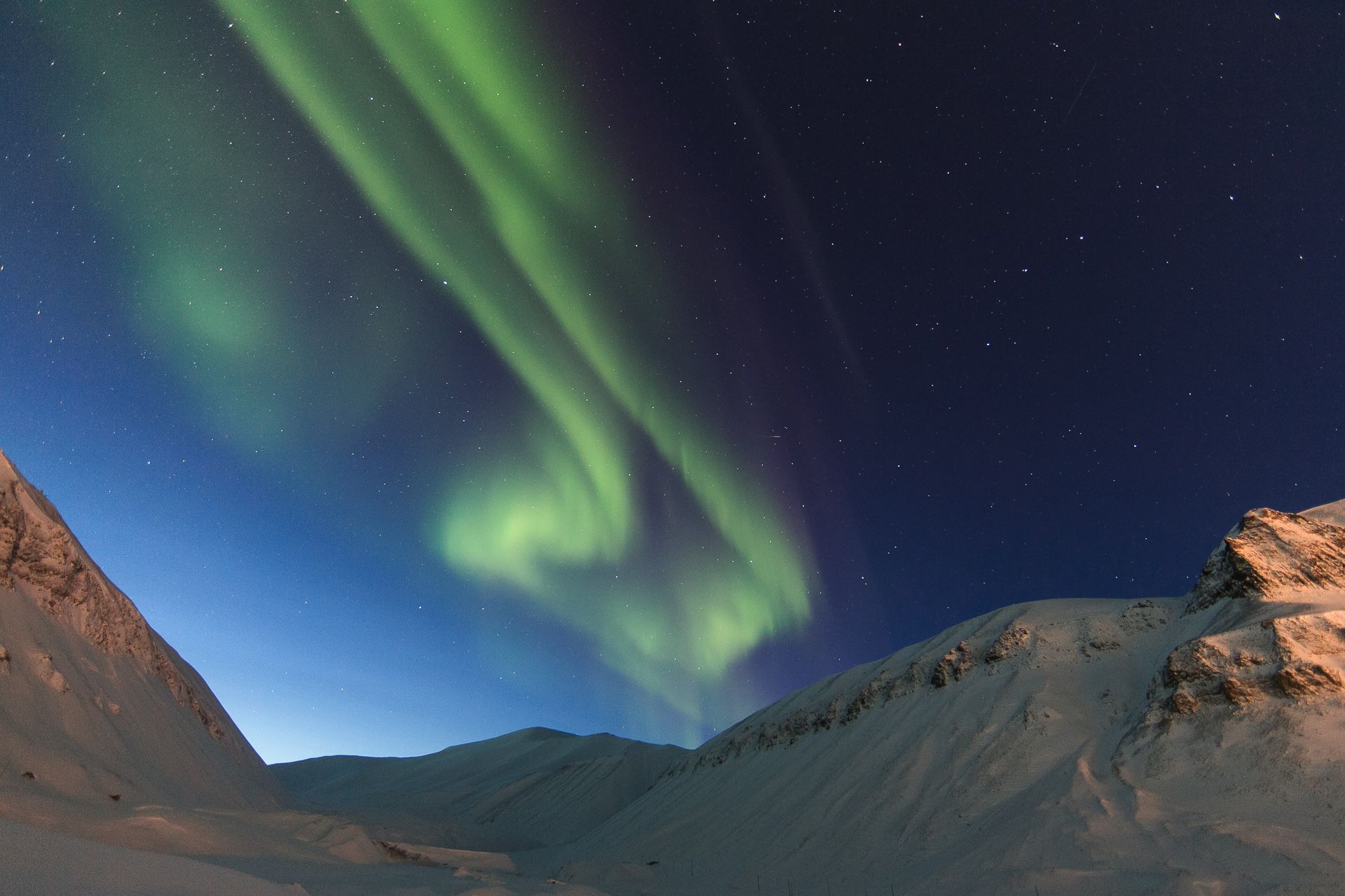 Et fjellandskap i forgrunnen med nordlys på himmelen i bakgrunnen