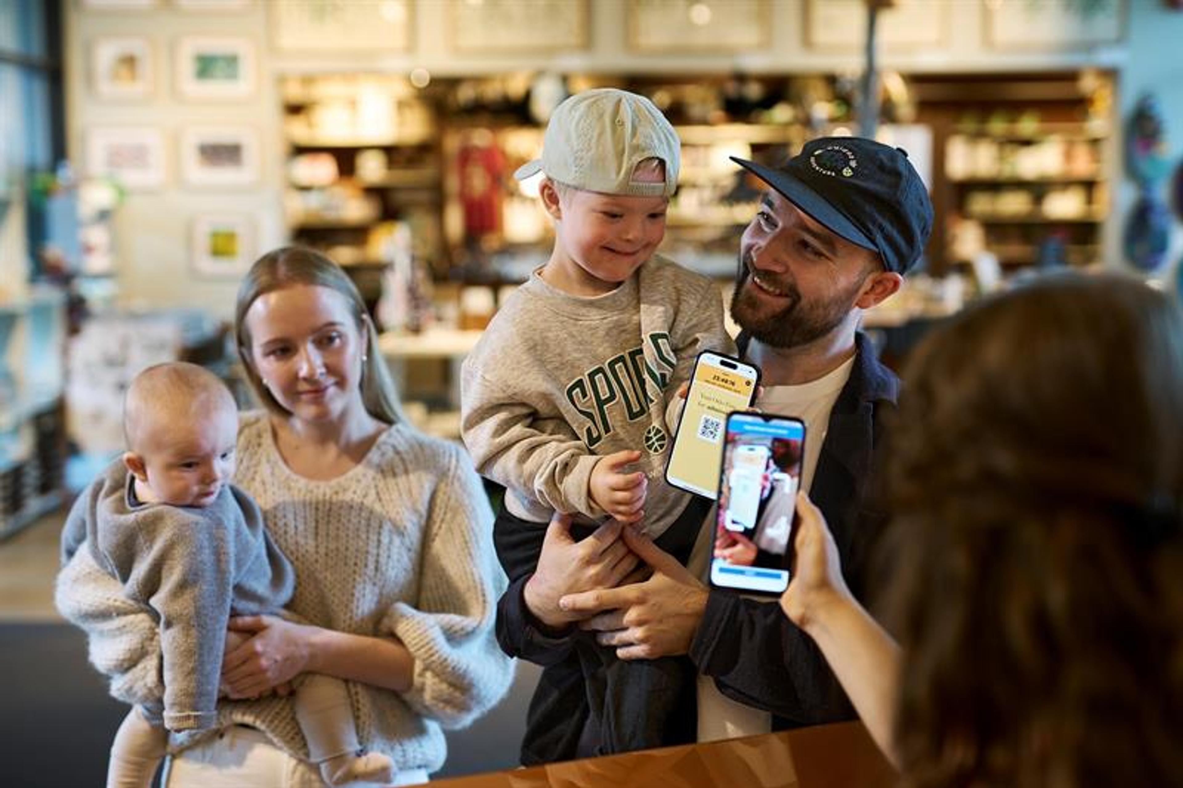 Mother and father each carrying a child and showing the Oslo Pass app to a museum staff member behind a counter.
