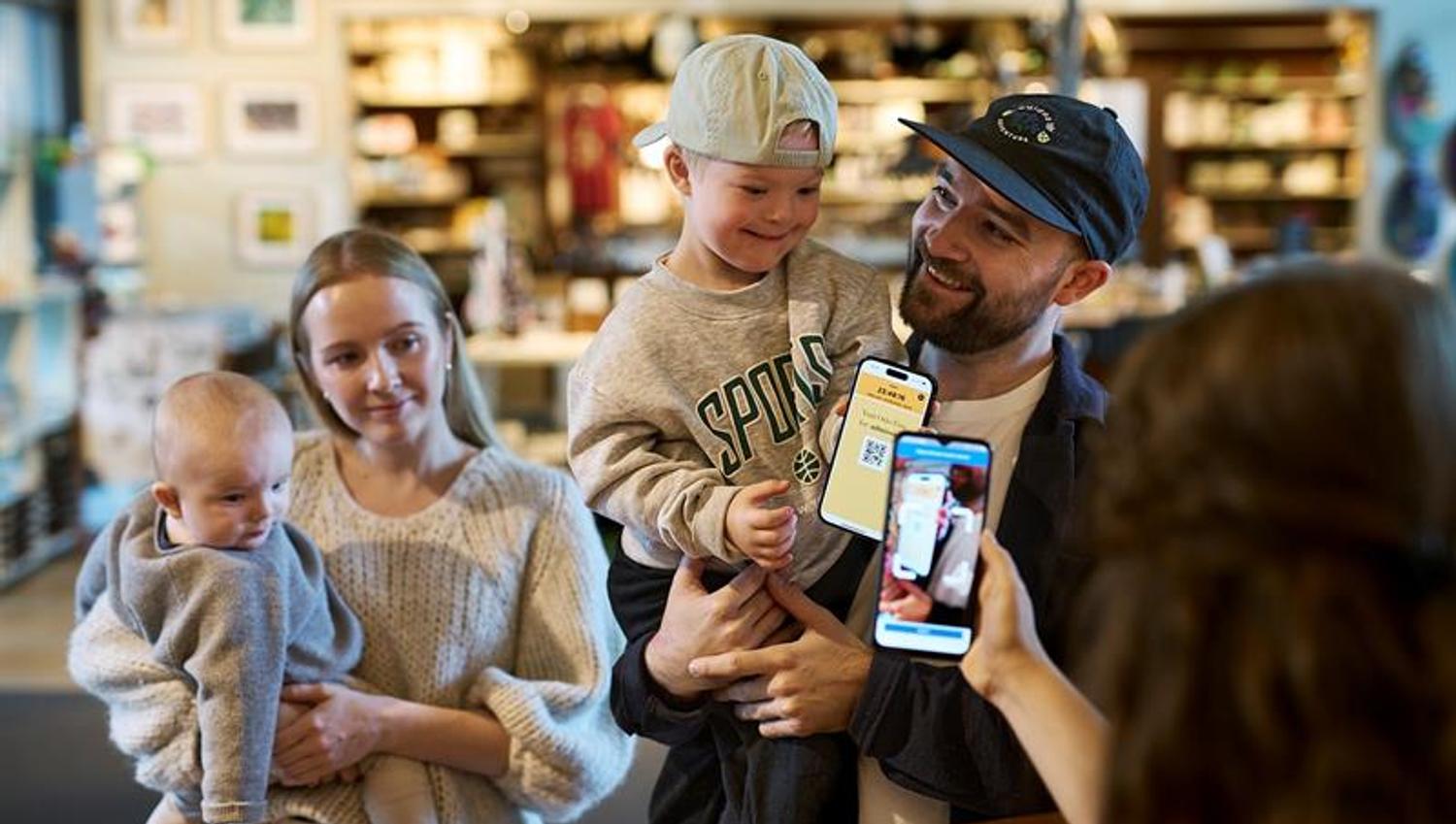 Mor og far som bærer hvert sitt barn og viser Oslo Pass-app til museumsansatt bak en skranke.