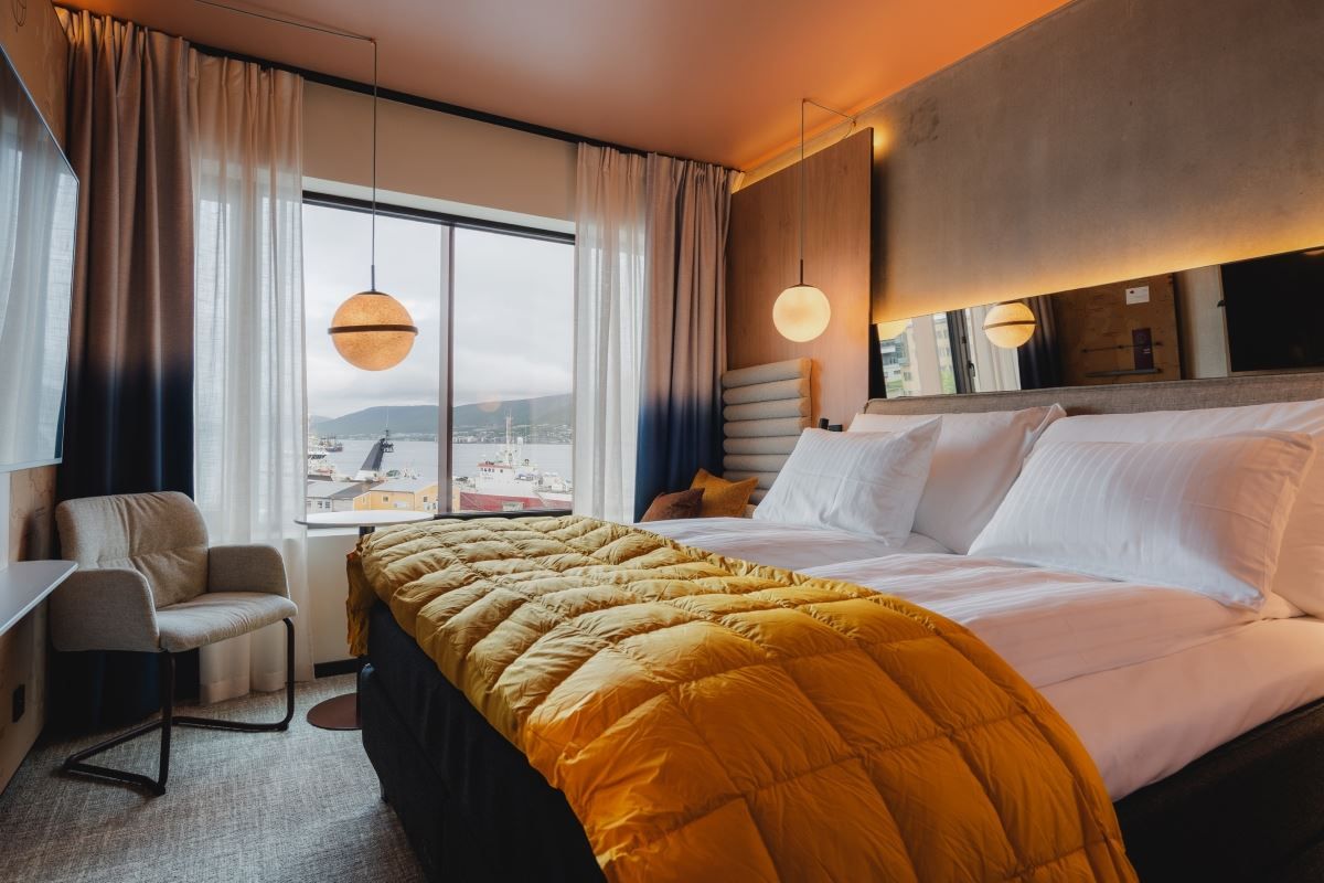 Bedroom with a view of water and boats, bed with white linens and a yellow blanket