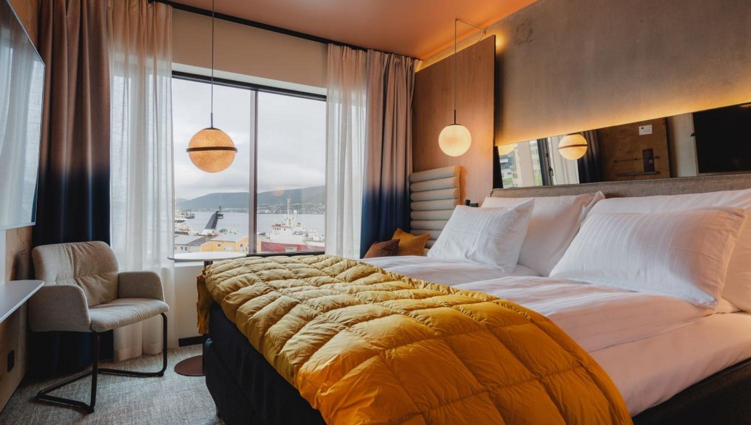 Bedroom with a view of water and boats, bed with white linens and a yellow blanket