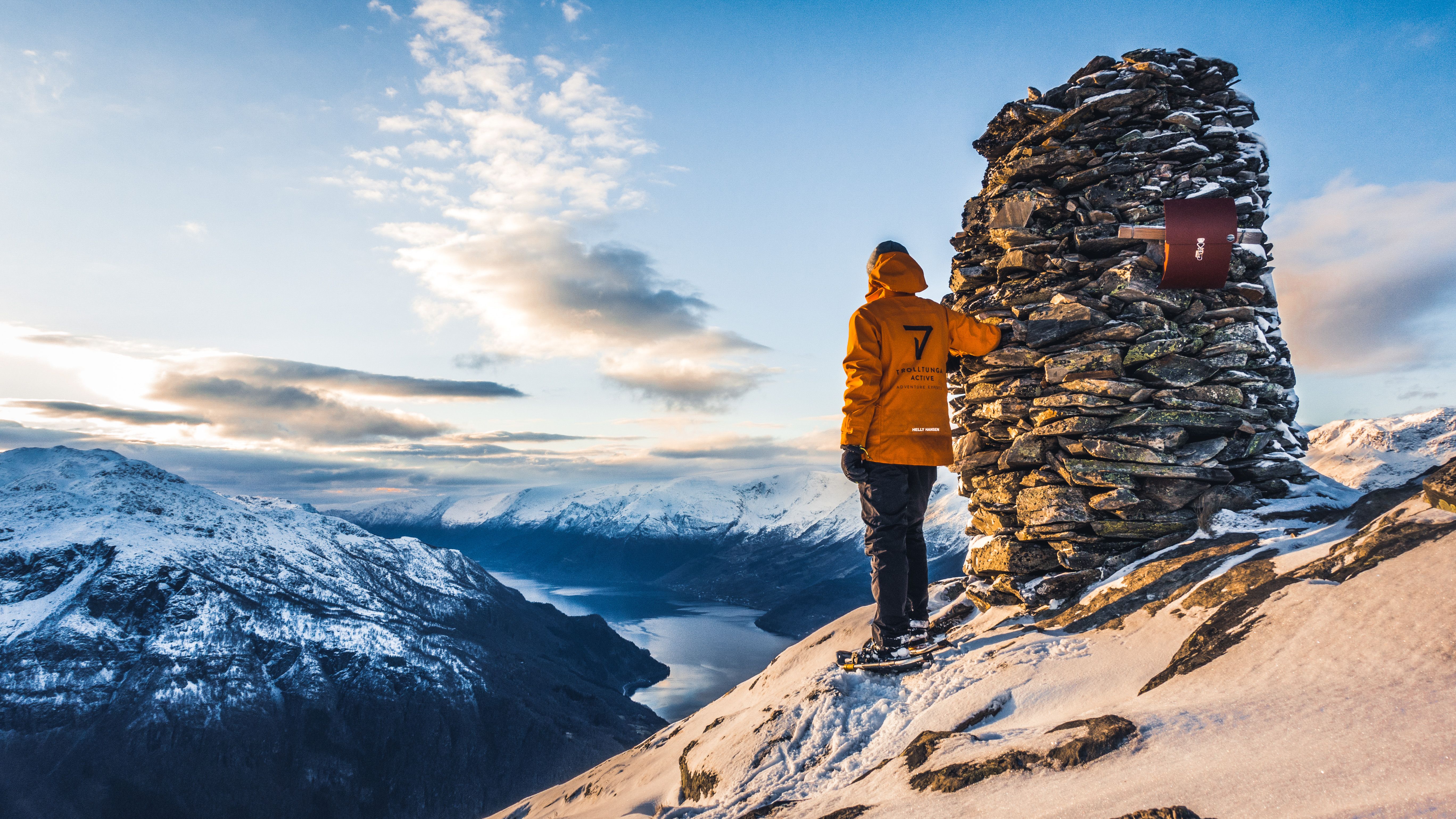 Snowshoer standing by a stone cairn overlooking fjord and winter mountains in Hardanger.