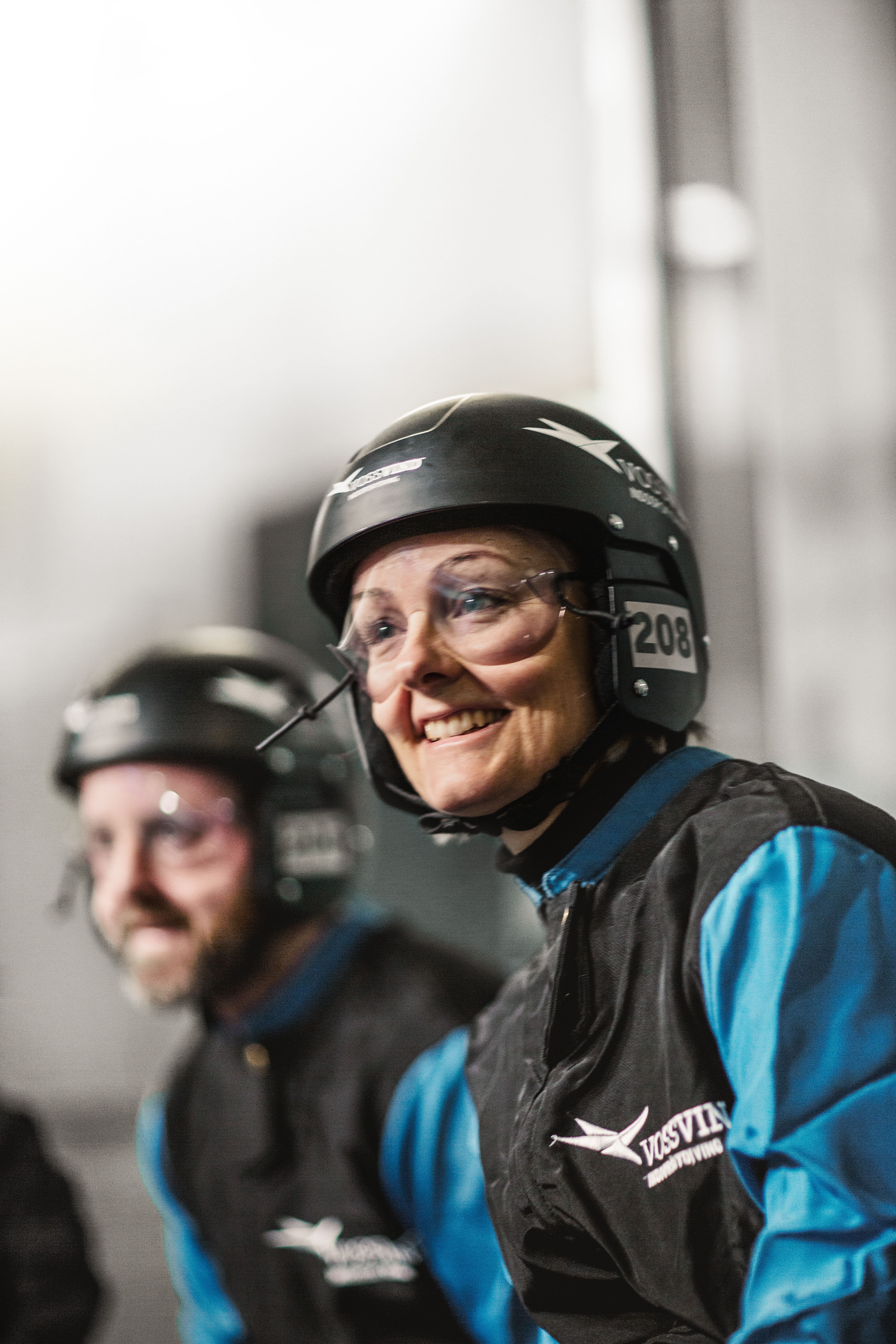 Smiling participant wearing helmet and goggles alongside others, preparing for an indoor flying session.