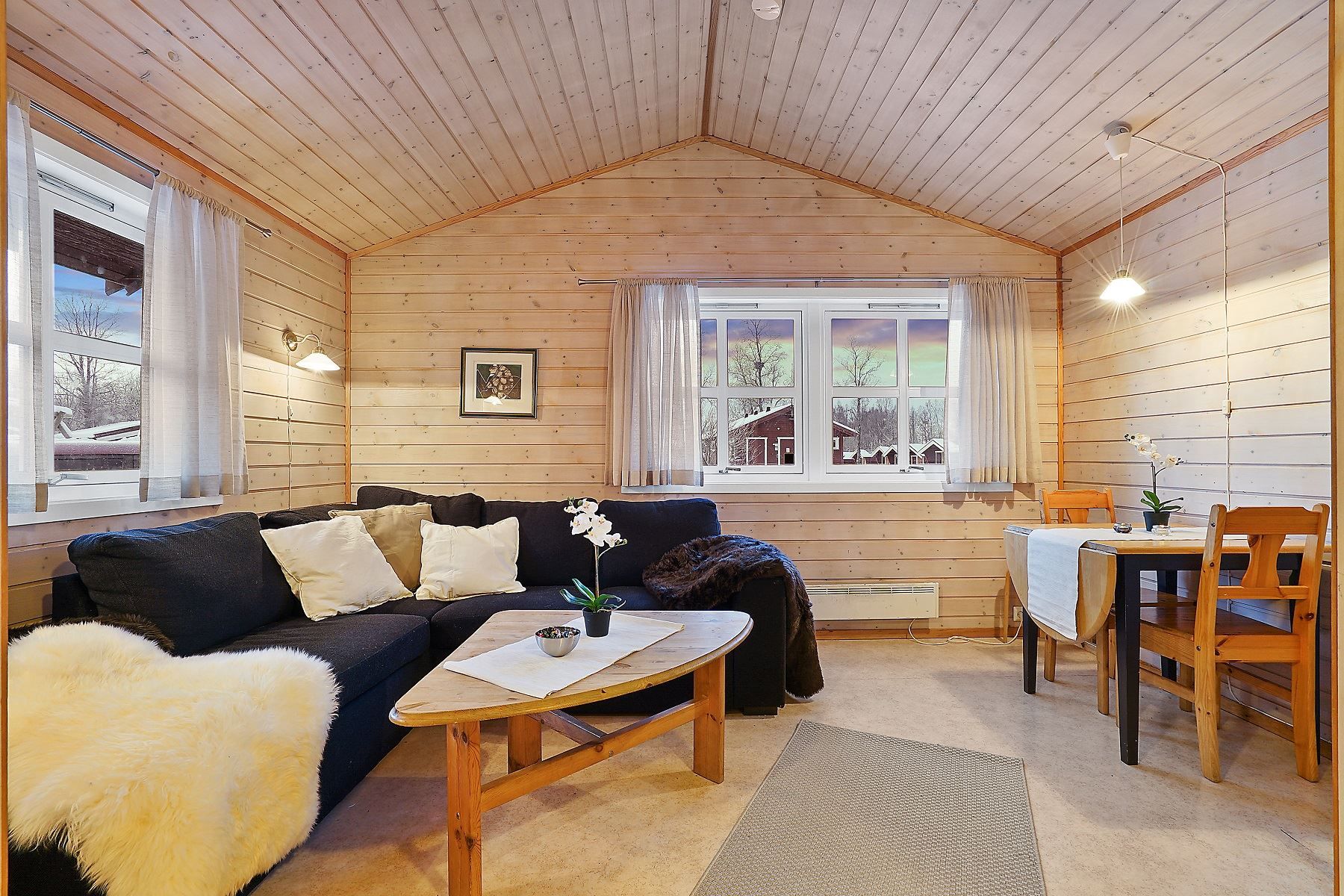 Living room with black sofa, dining table for two, and large windows with curtains