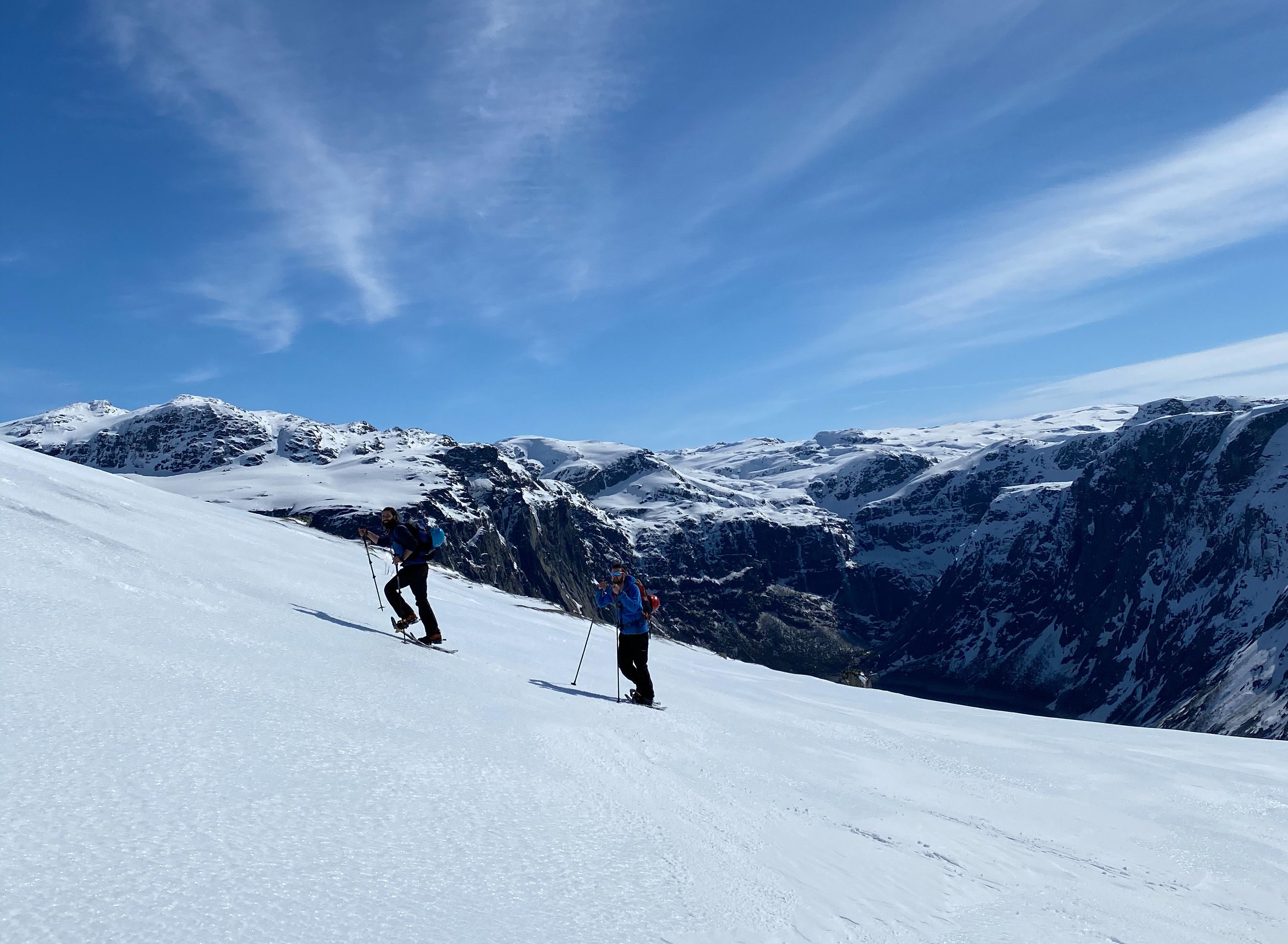 Two snowshoe hikers climbing in steep terrain with fjord views near Trolltunga.