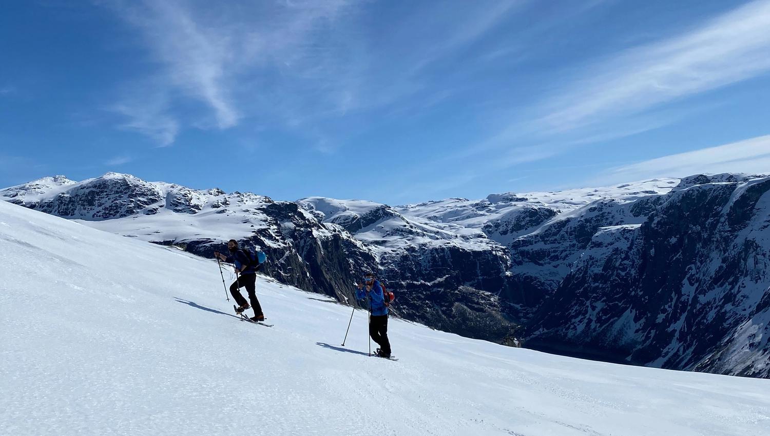 Two snowshoe hikers climbing in steep terrain with fjord views near Trolltunga.