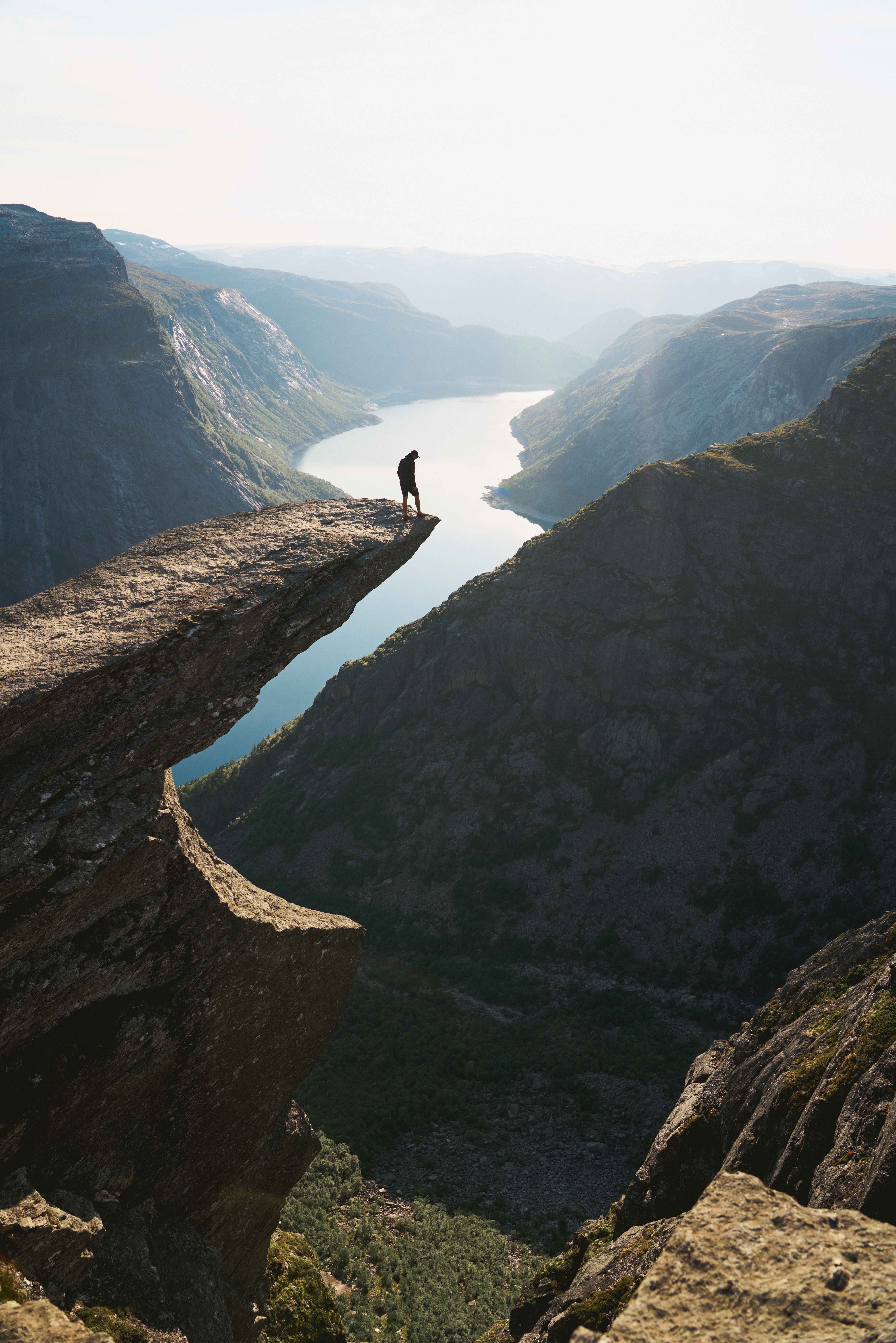 En person står alene på Trolltunga med utsikt over fjorden på en klar dag.