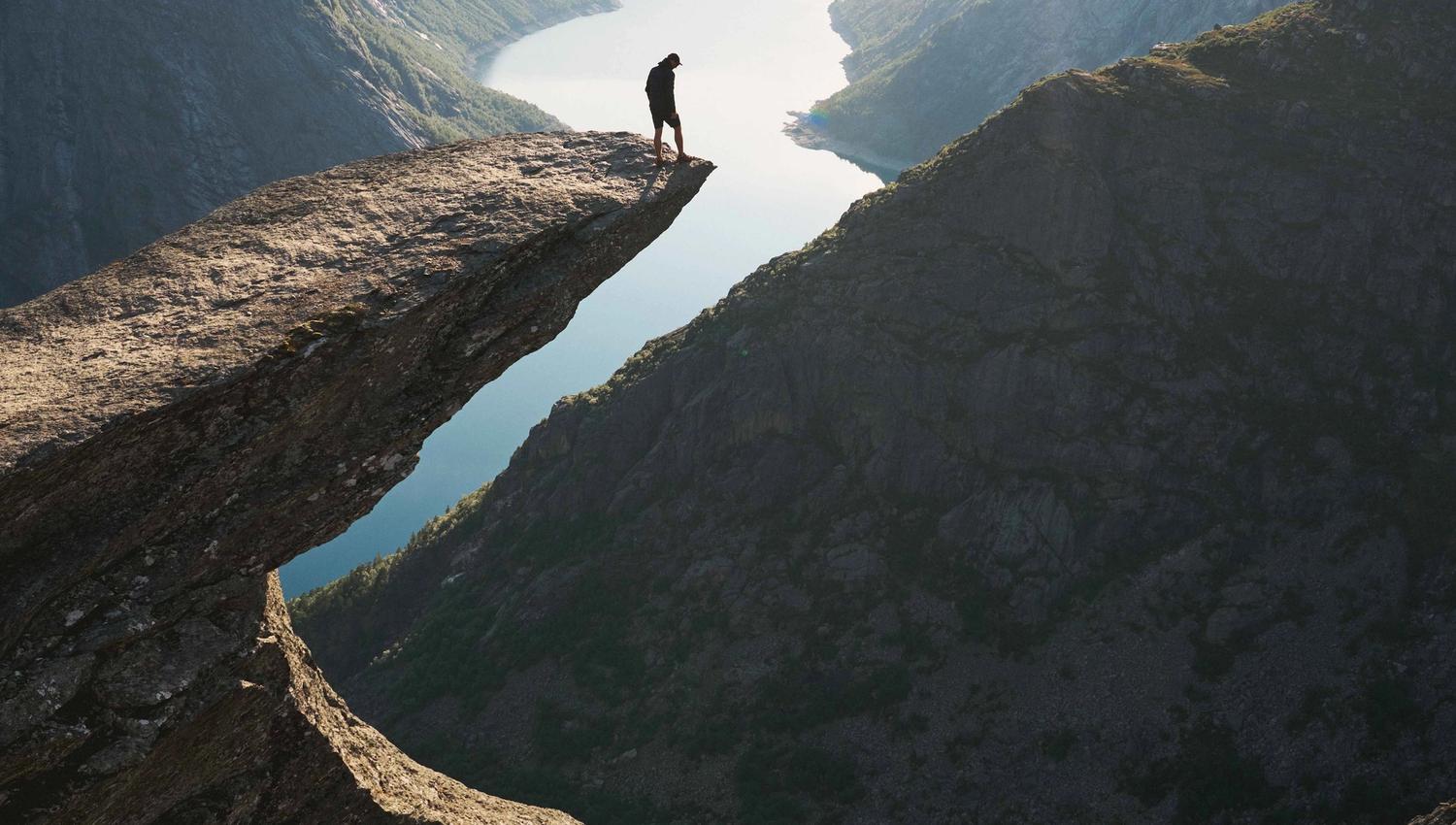 En person står alene på Trolltunga med utsikt over fjorden på en klar dag.