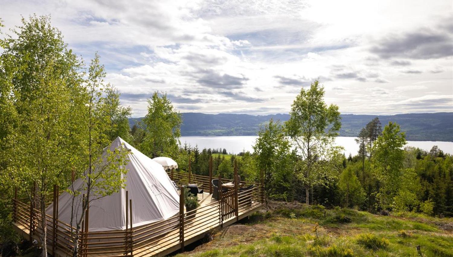 Et telt plassert i et grønt skogsterreng med utsikt mot en innsjø.