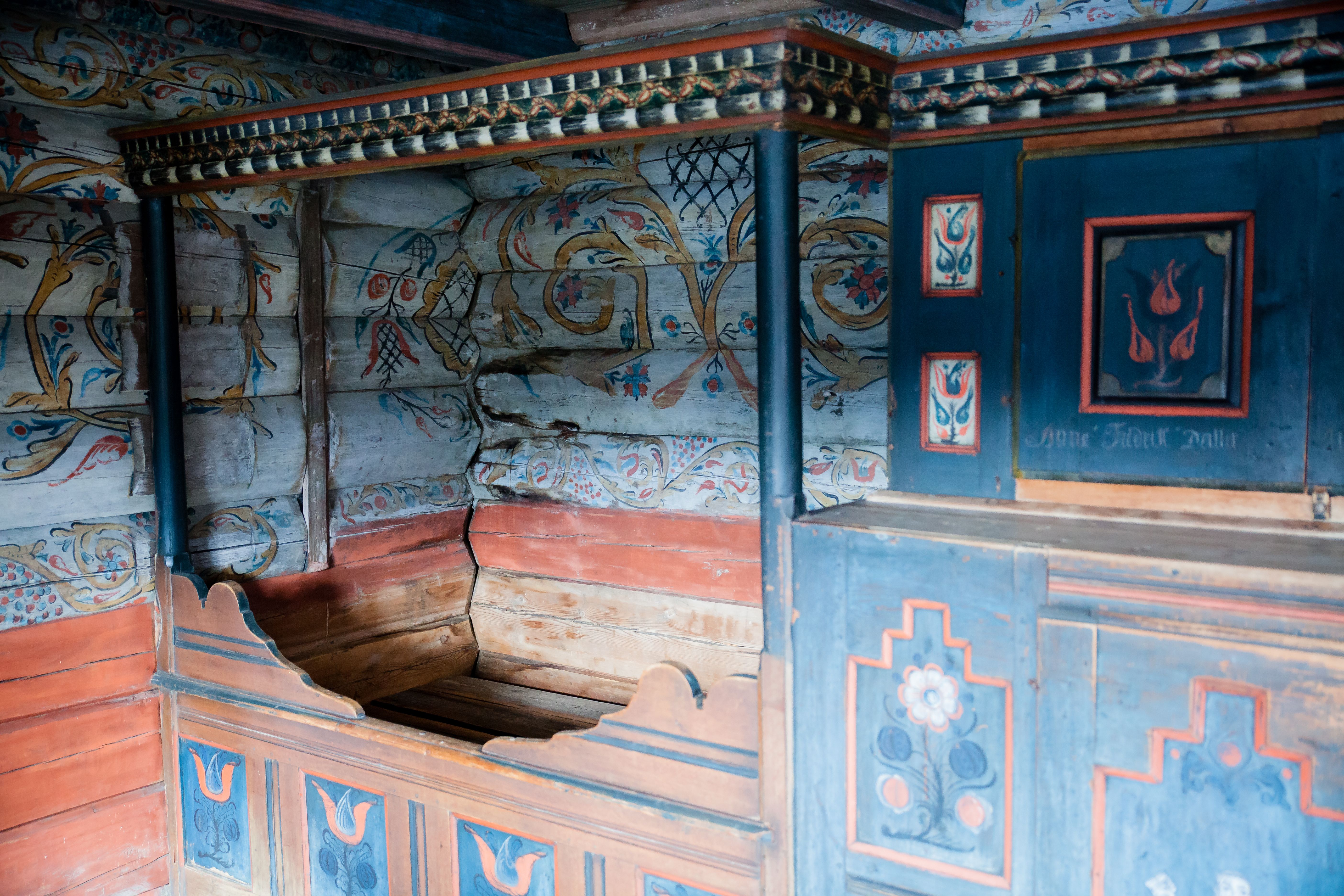 Marnardal Museum og Mjålandsstova, treseng  med blå skap vedsidenav. Hvitmalte tømmervegger med fargerike detaljer i rosemaling.