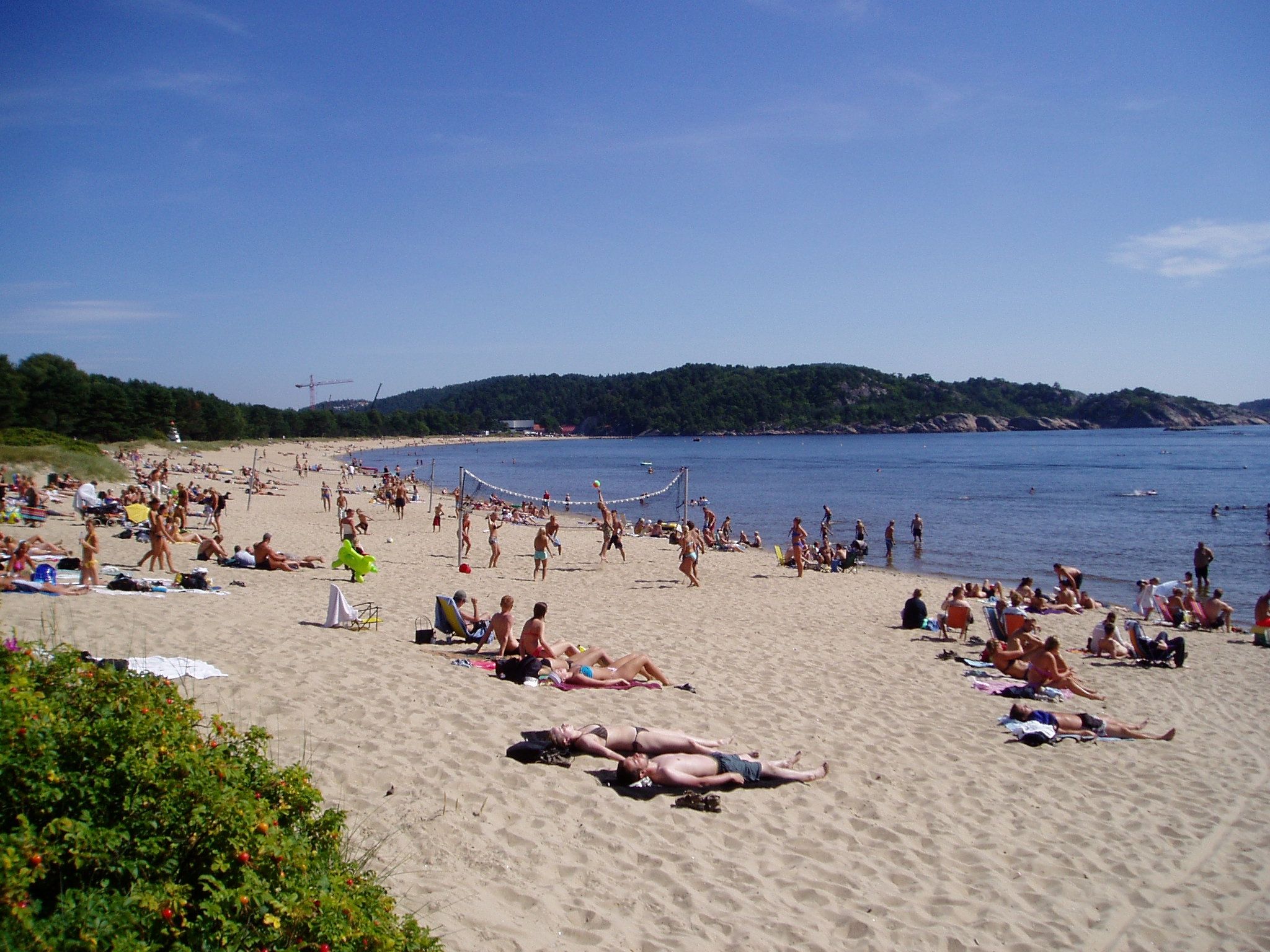 Mange mennesker som soler seg på stranden, mens noen spiller strandvolleyball
