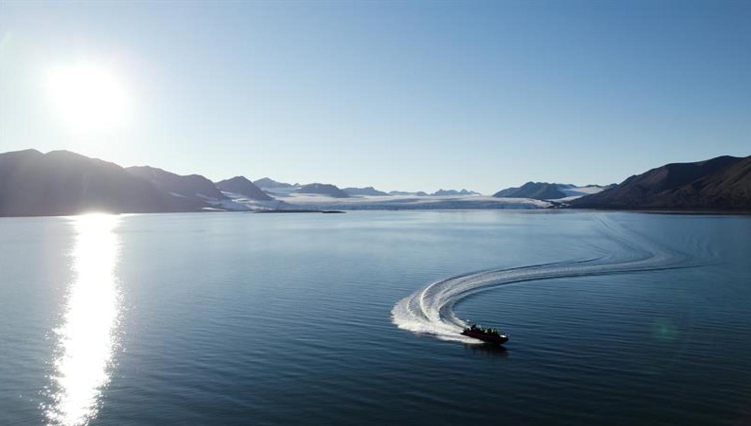 Båt kjører over en stille fjord i solskinn.