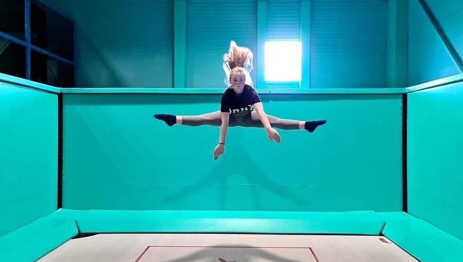 Jente som gjør splitthopp på en trampoline. Foto.