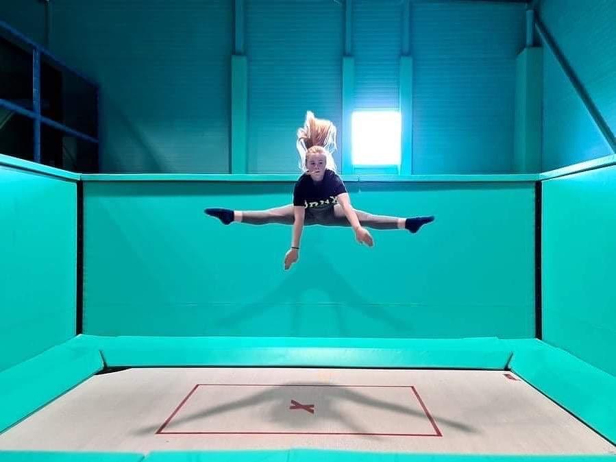 Girl doing a split jump on a trampoline. Photo.