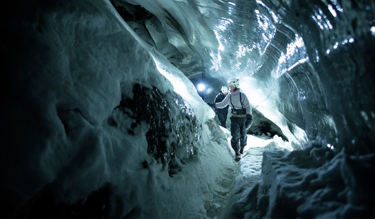 A guide with a helmet and headlamp showing guests the way through a dark ice cave