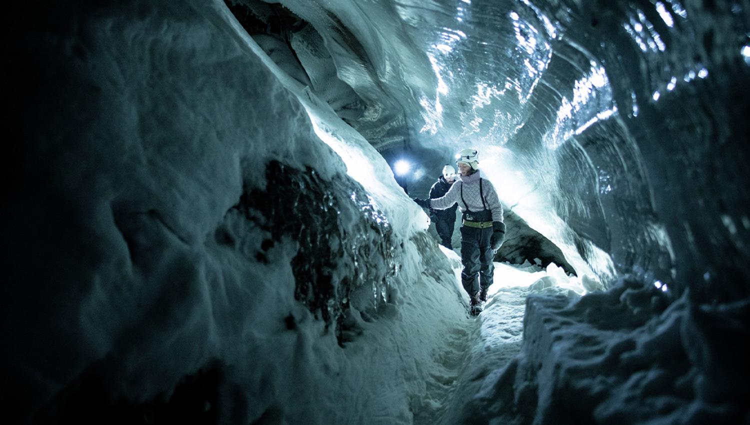 A guide with a helmet and headlamp showing guests the way through a dark ice cave