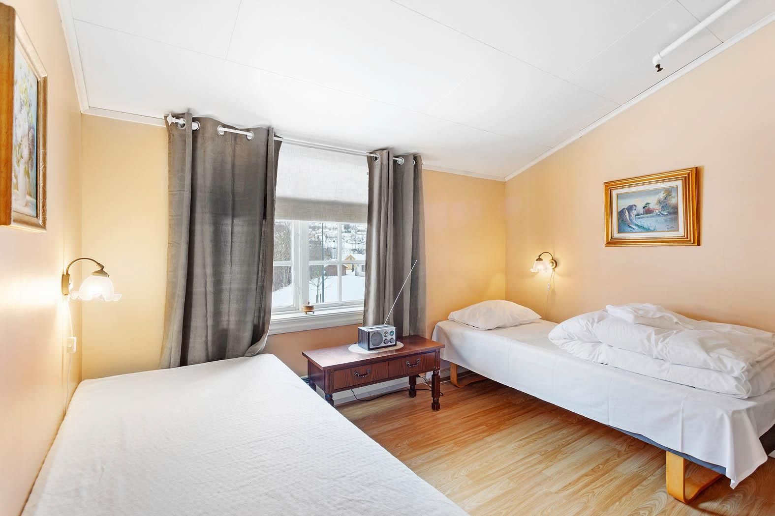 Lyst soverom med to enkle senger og utsikt mot bygda på Jaunsen Gjestgjevarstad.