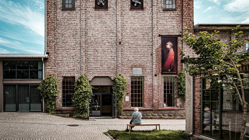 Nærbilde av museumsbygget. En person sitter på en benk.