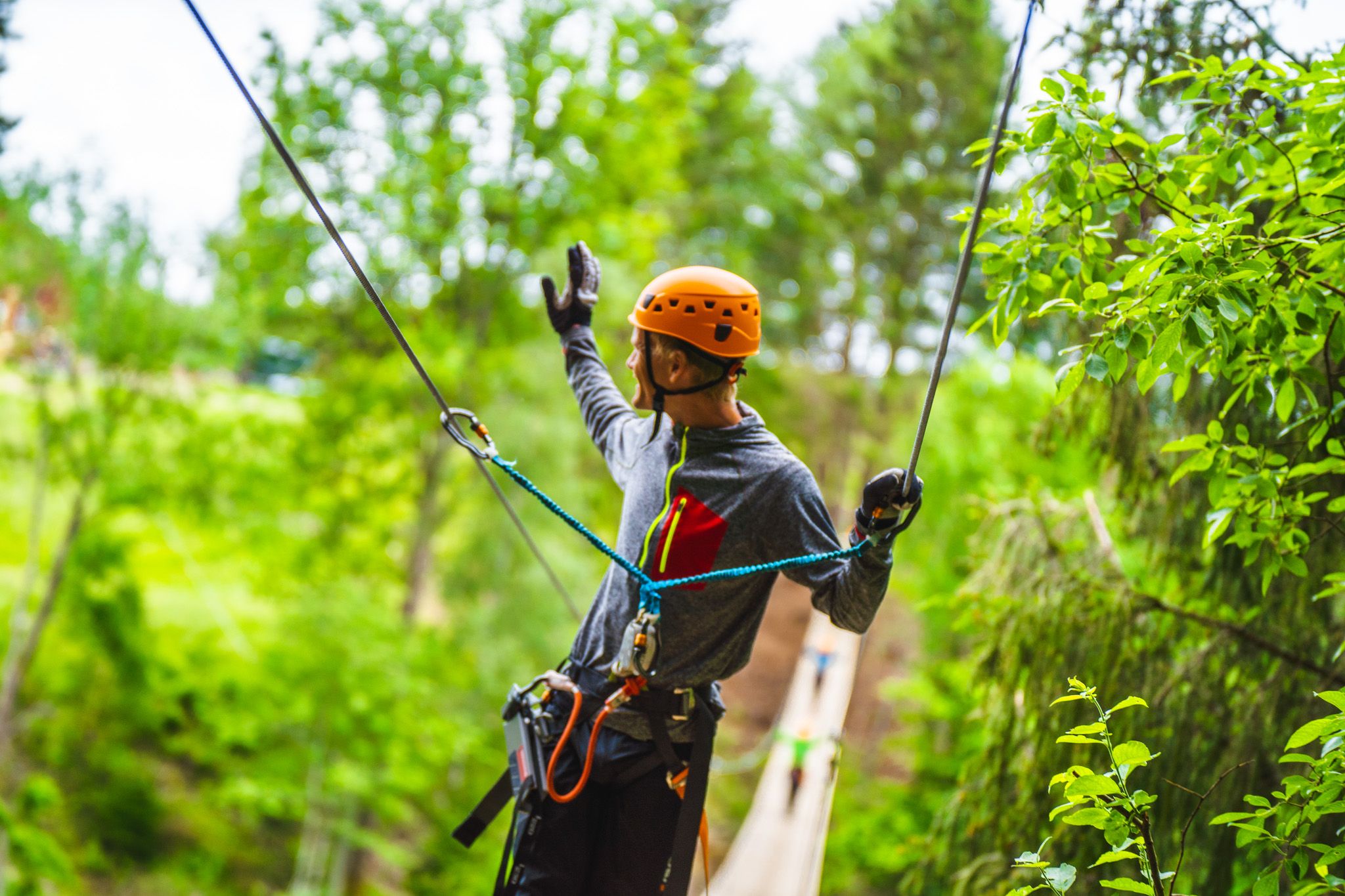En mann har kommet seg over hengebroa og vinker over til andre siden i Via ferrata Haldenkanalen