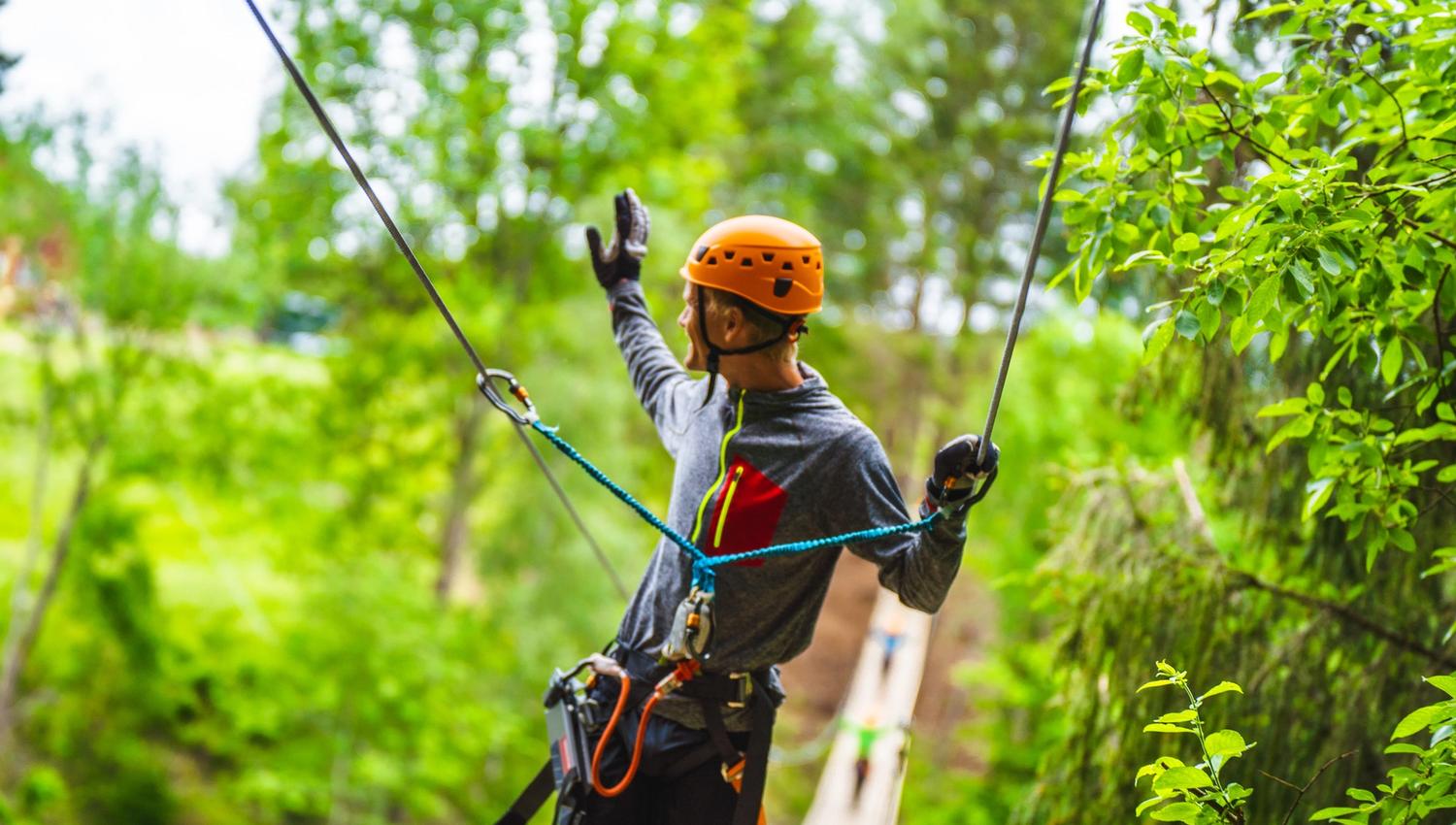 En mann har kommet seg over hengebroa og vinker over til andre siden i Via ferrata Haldenkanalen