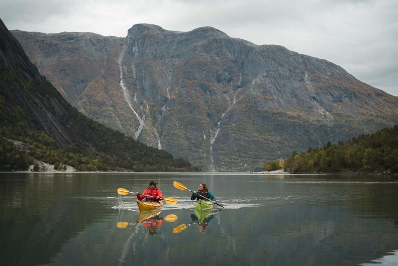 A couple kayakking on the fjord with a tall mountain in the background.