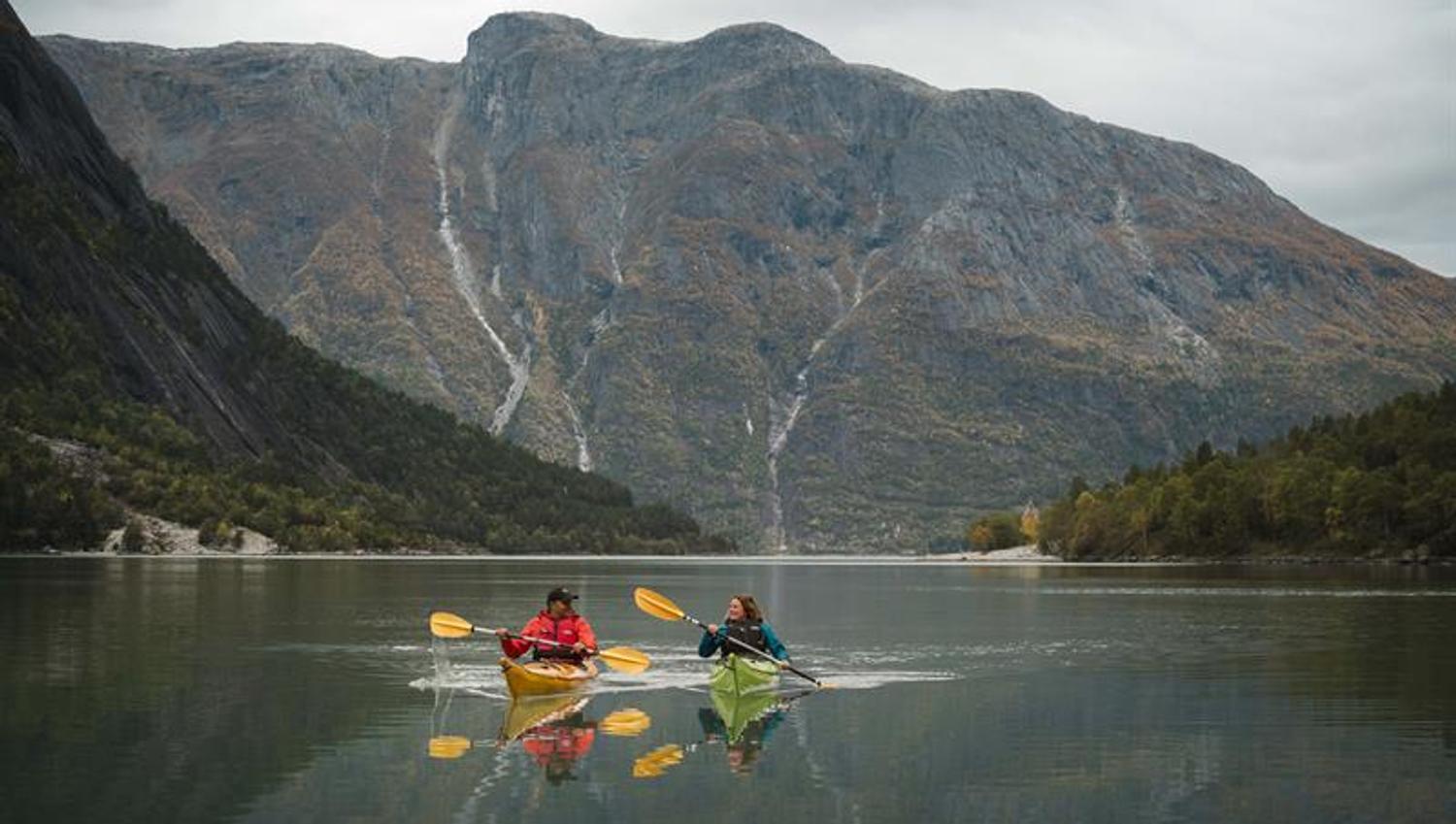 A couple kayakking on the fjord with a tall mountain in the background.