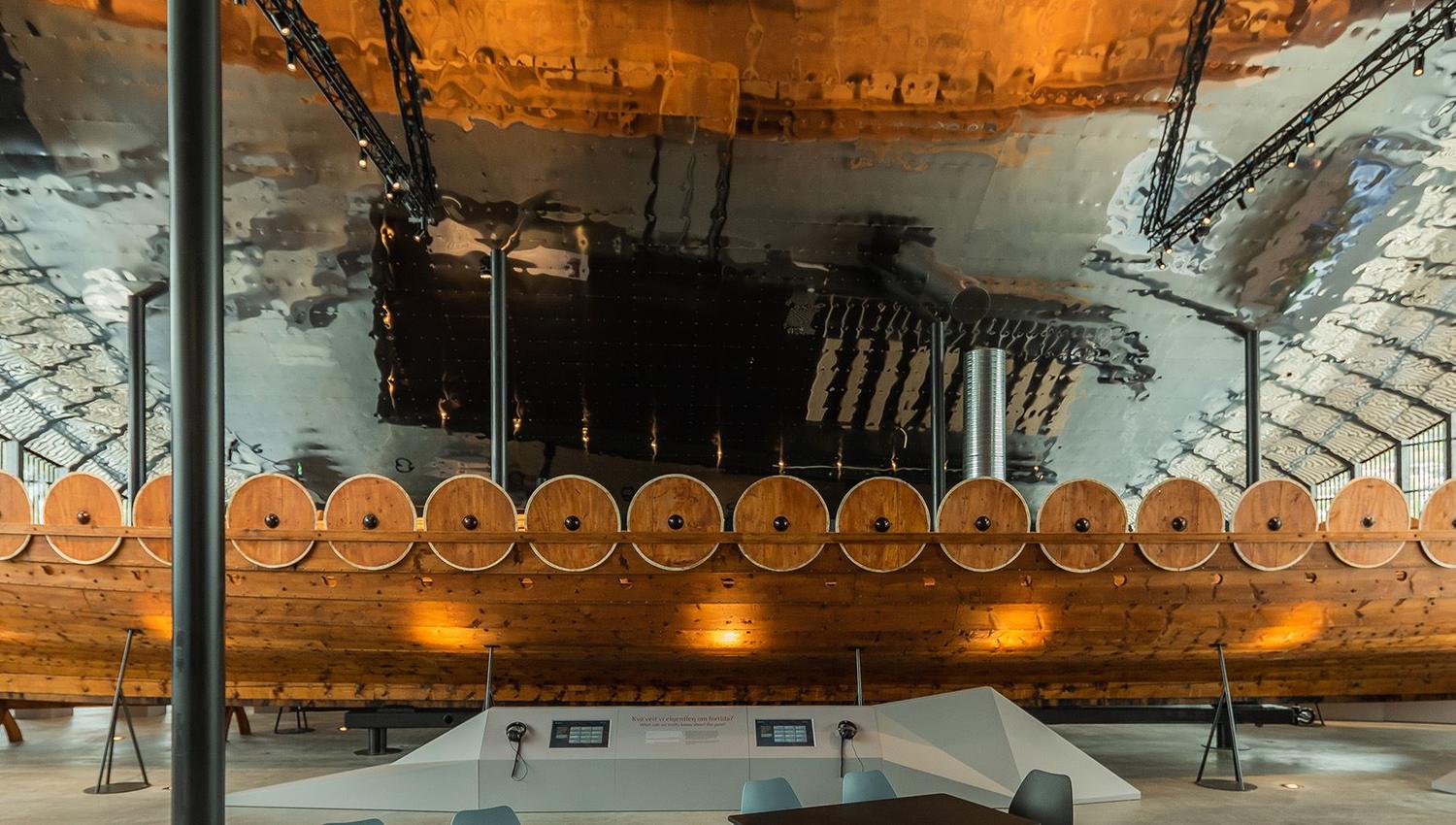 Det 30 meter lange Myklebustskipet utstilt inne på Sagastad Vikingsenter - Eit stort vikingskip i tre står utstilt innandørs i ein museumsal med metalltak, vindauge og lyspunkter..