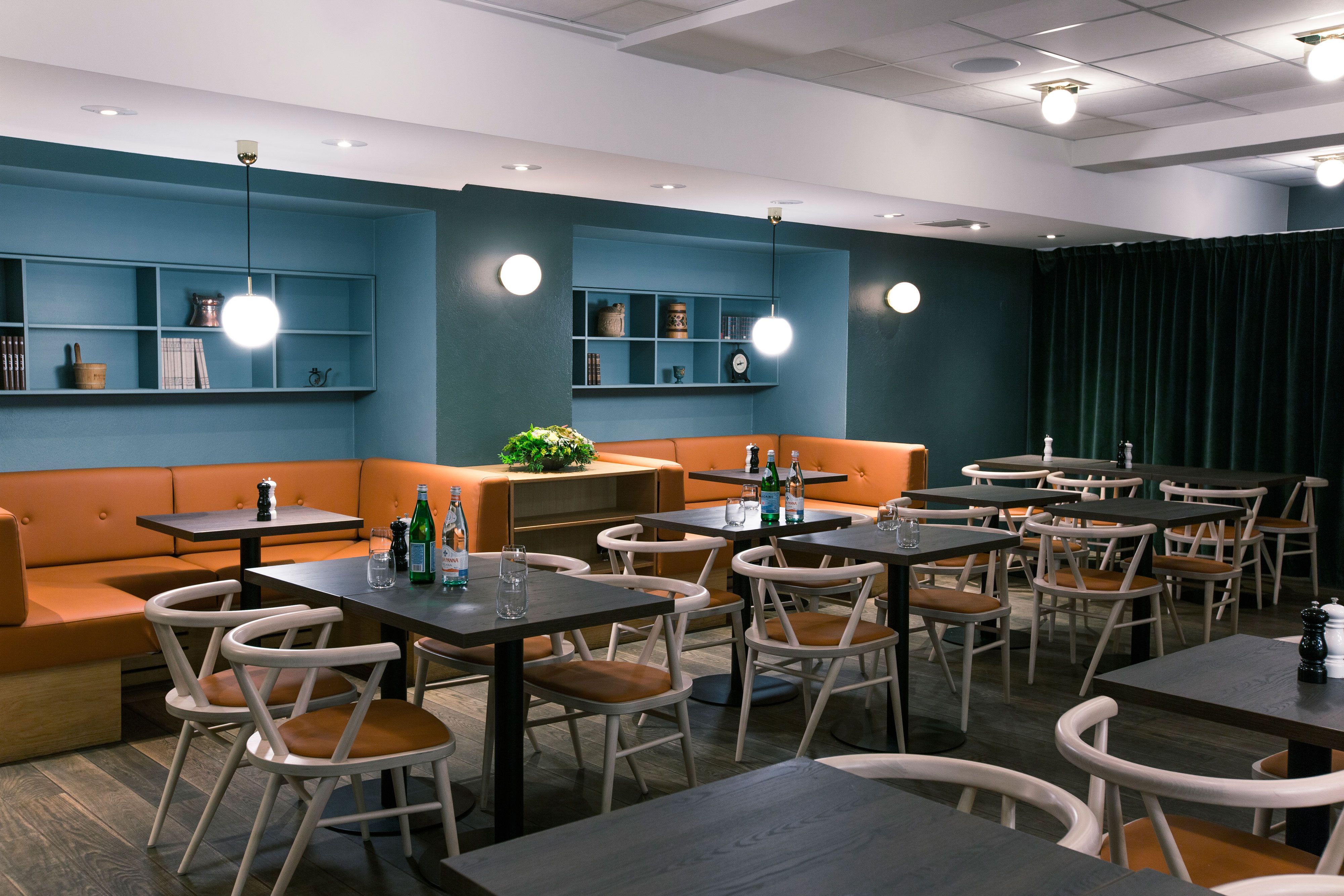 Interiør med bord, stoler og sitteseksjoner, blå vegger.