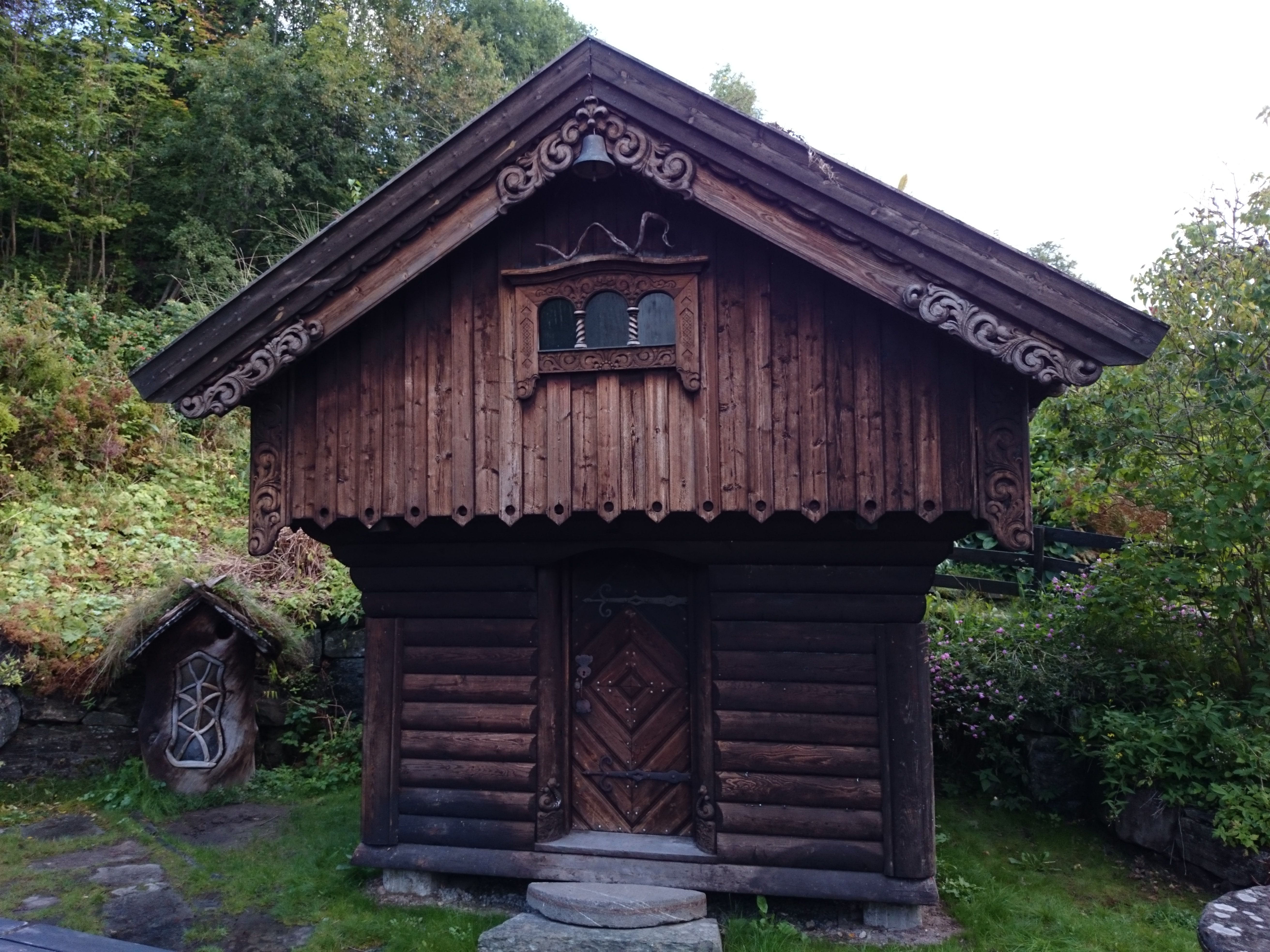 Vakkert utskore stabbur i tradisjonell stil i hagen til Ullensvang Gjesteheim, omringa av grøne vekstar.