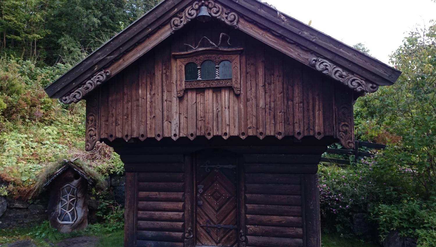 Vakkert utskore stabbur i tradisjonell stil i hagen til Ullensvang Gjesteheim, omringa av grøne vekstar.