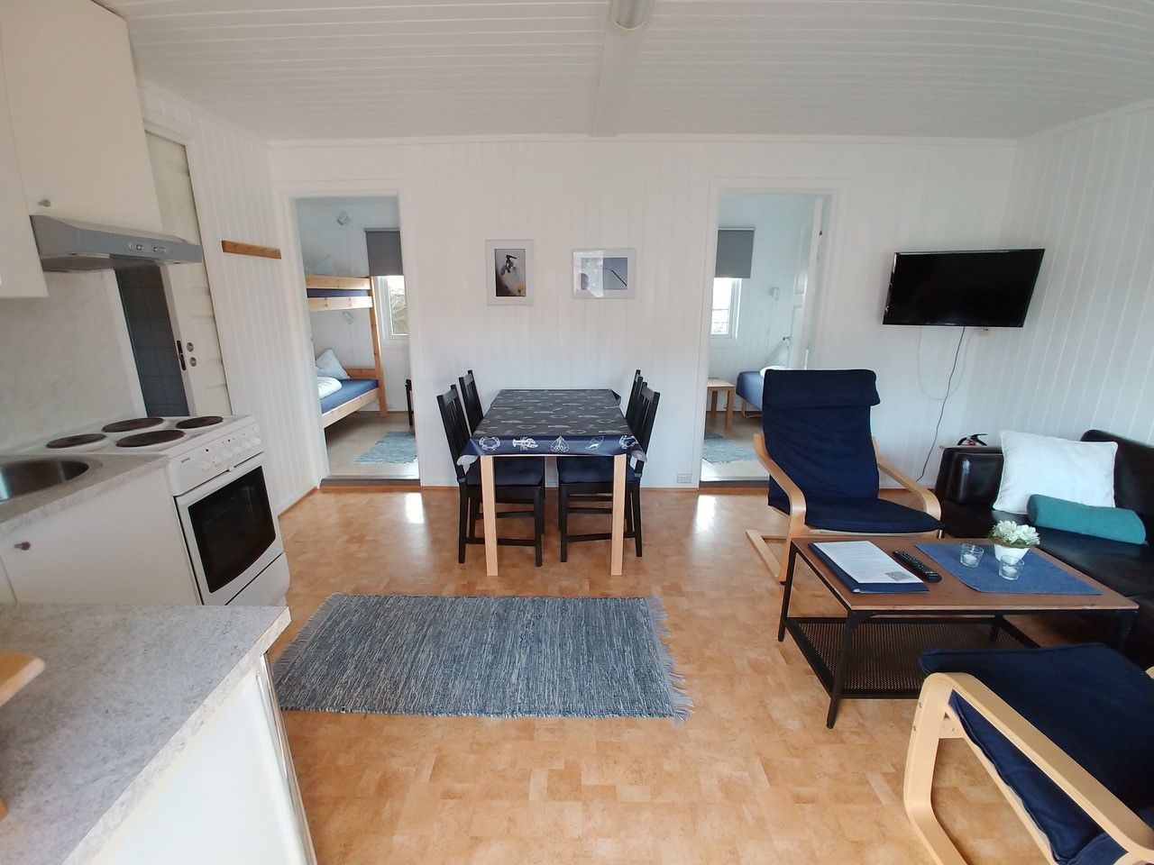 Stue med sofa, stoler, bord, kjøkkenbord og kjøkkenstoler, kjøkken krok og sikt til soverommene