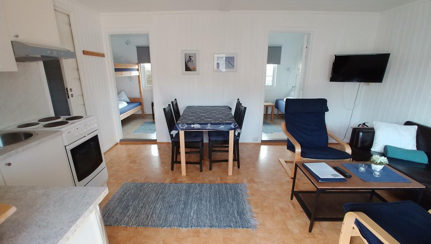 Stue med sofa, stoler, bord, kjøkkenbord og kjøkkenstoler, kjøkken krok og sikt til soverommene