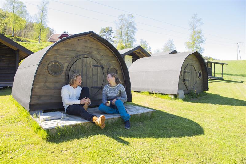 Par som sitter foran en av hobbit hyttene på Adventure Norway og slapper av i finværet.