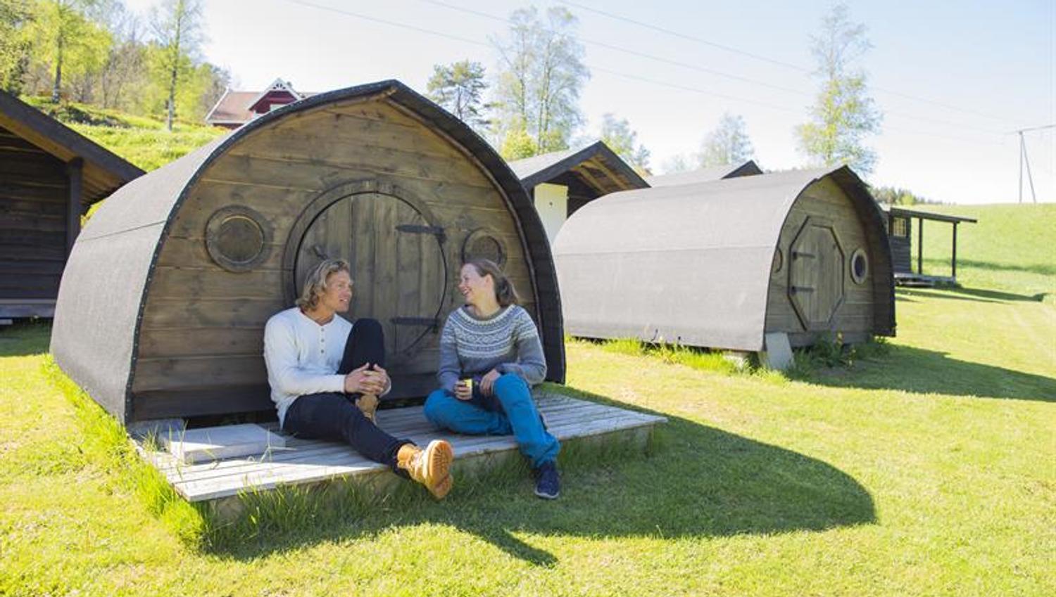 Par som sitter foran en av hobbit hyttene på Adventure Norway og slapper av i finværet.