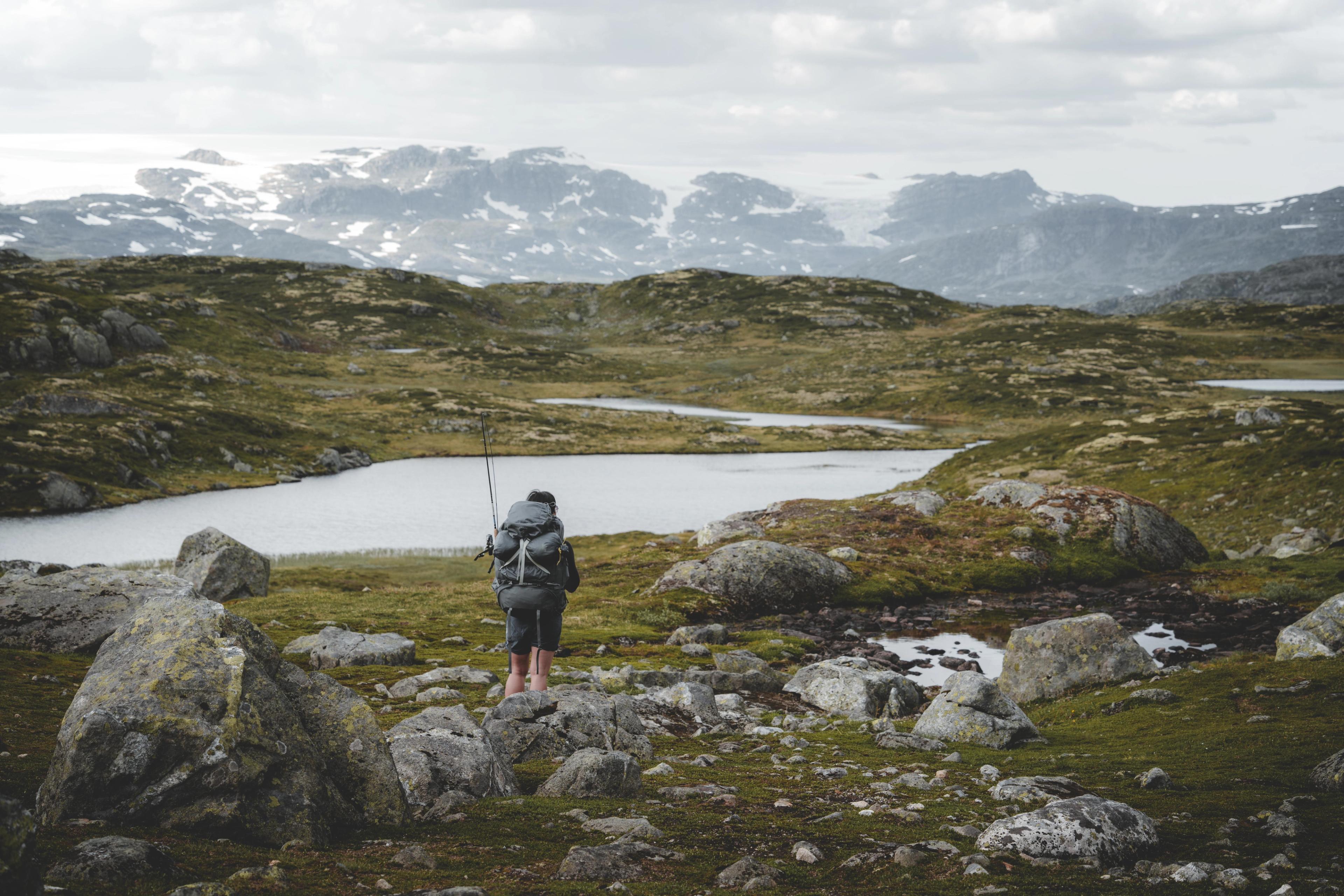 En kvinne med ryggsekk og fiskestang. Fjellvann og fjell i bakgrunnen.
