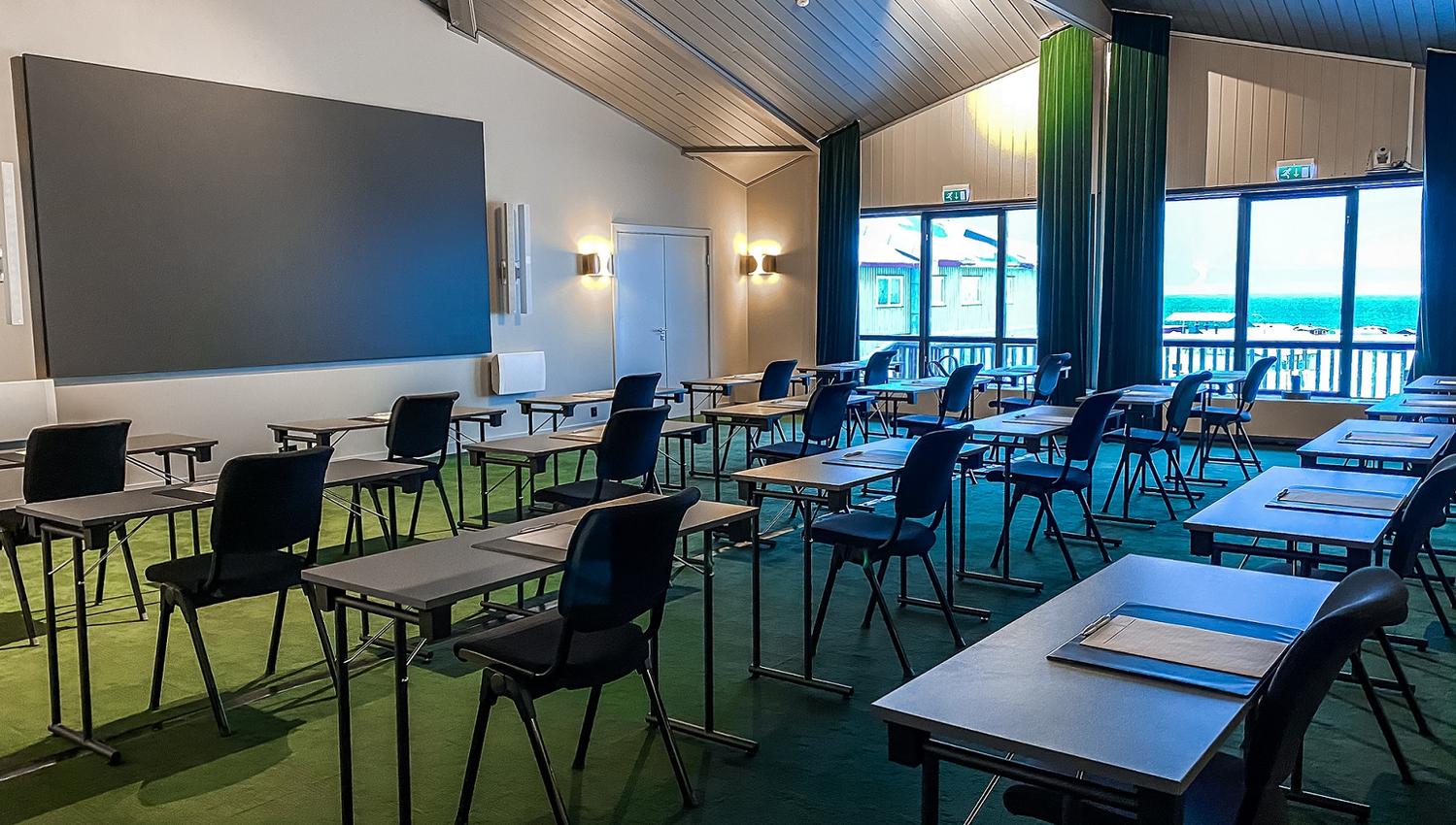 A large conference room set up with chairs and tables facing a large screen